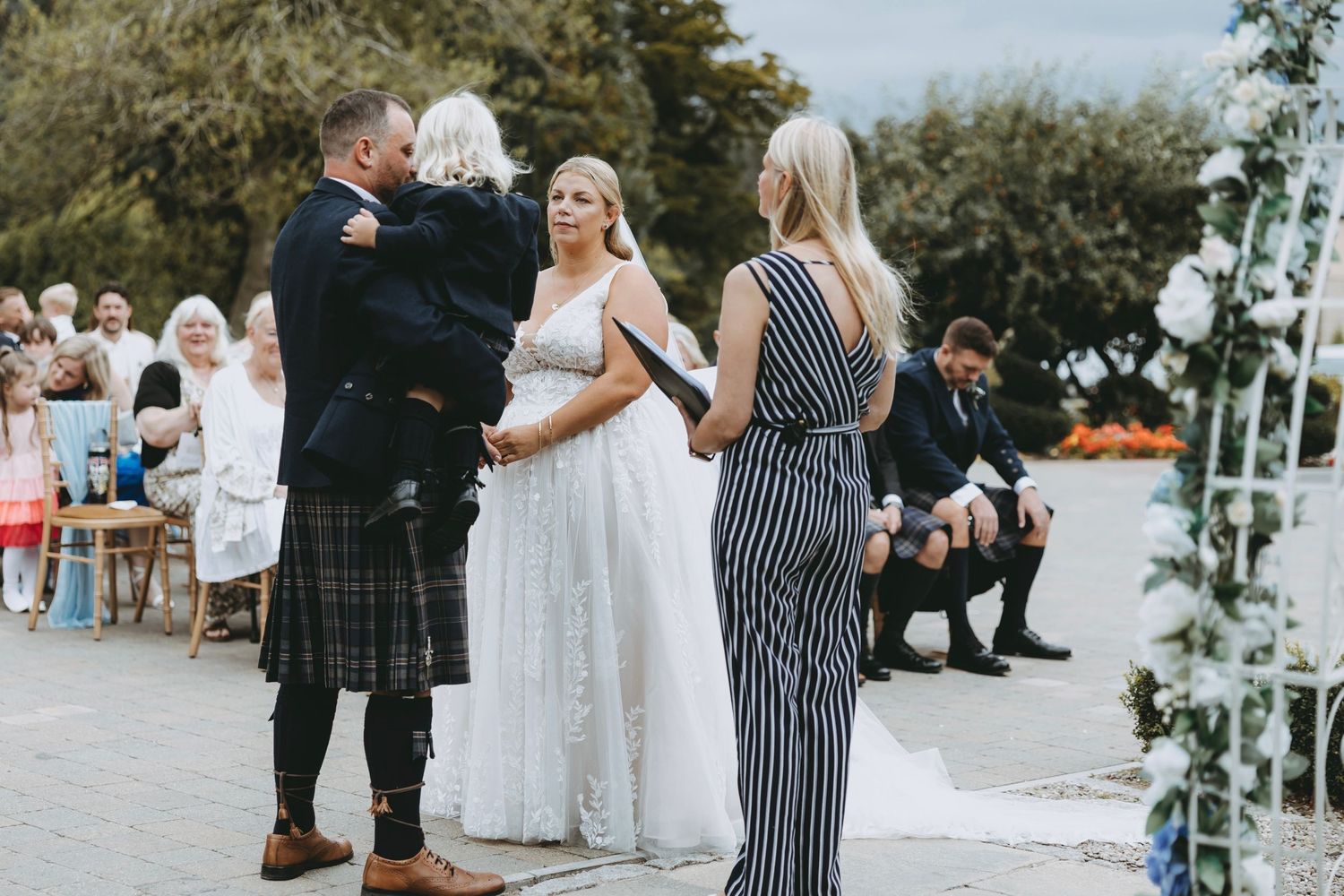 Outdoor wedding venue decorated with white floral arrangements and stone pathway.