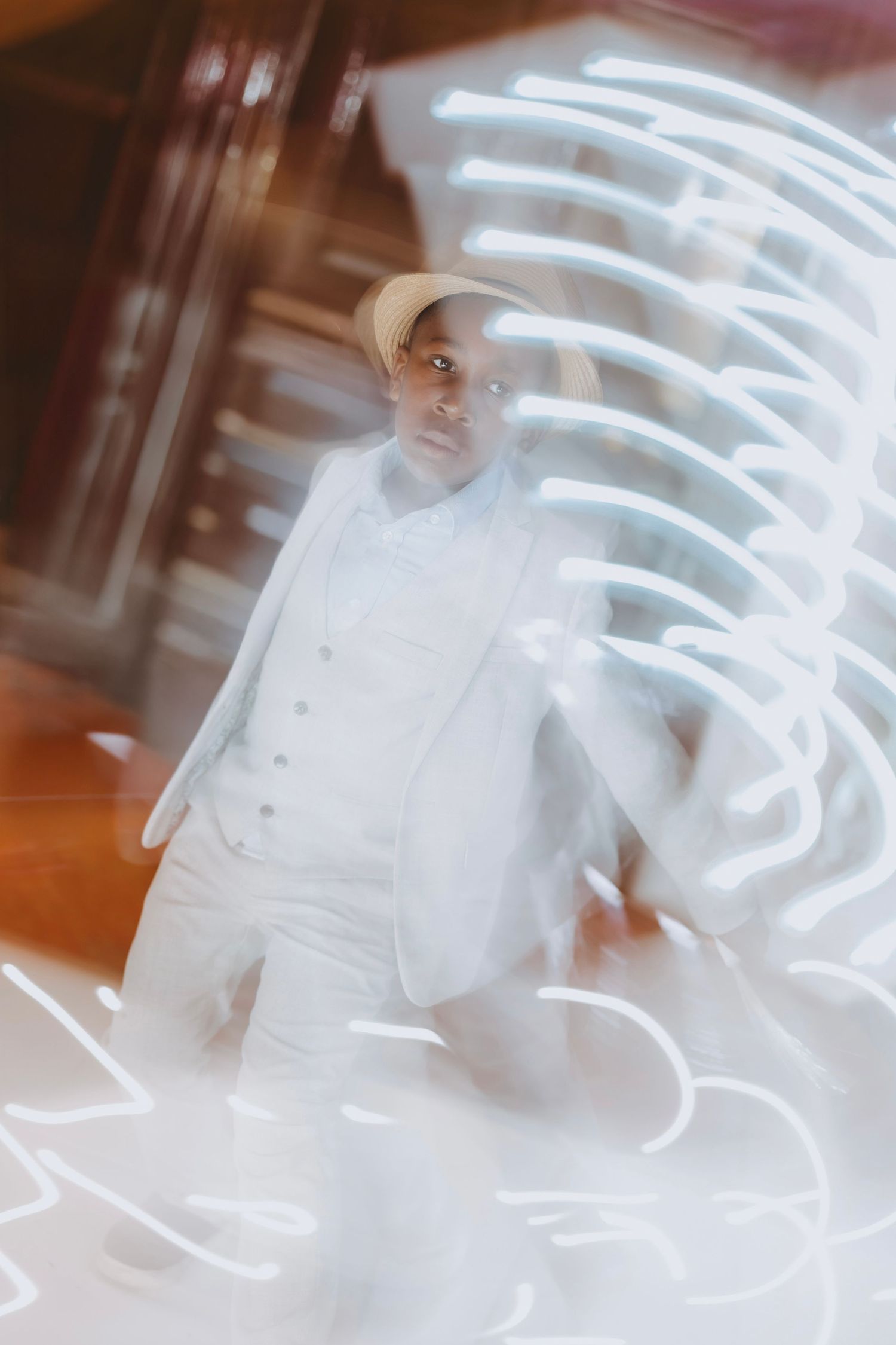 Man in white suit and cap poses dramatically with swirling light trails in a long exposure artistic photo.