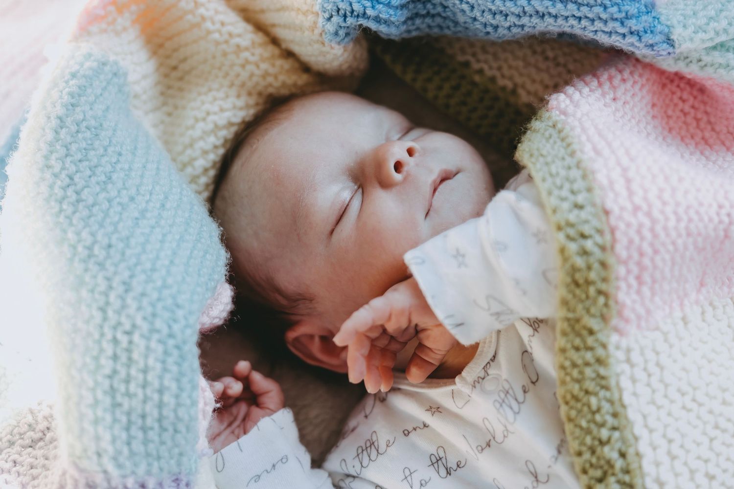 A sleeping baby wrapped in a cozy knit blanket with soft pastel colors.