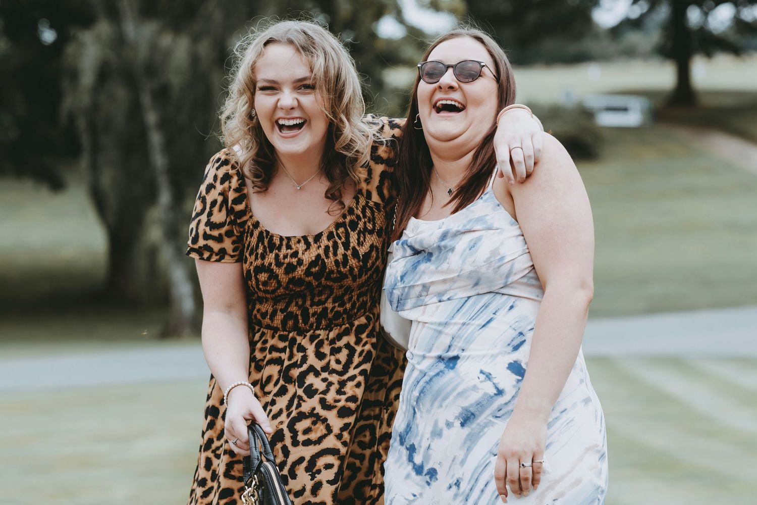 Two friends wearing contrasting leopard print and tie-dye dresses pose together outdoors.