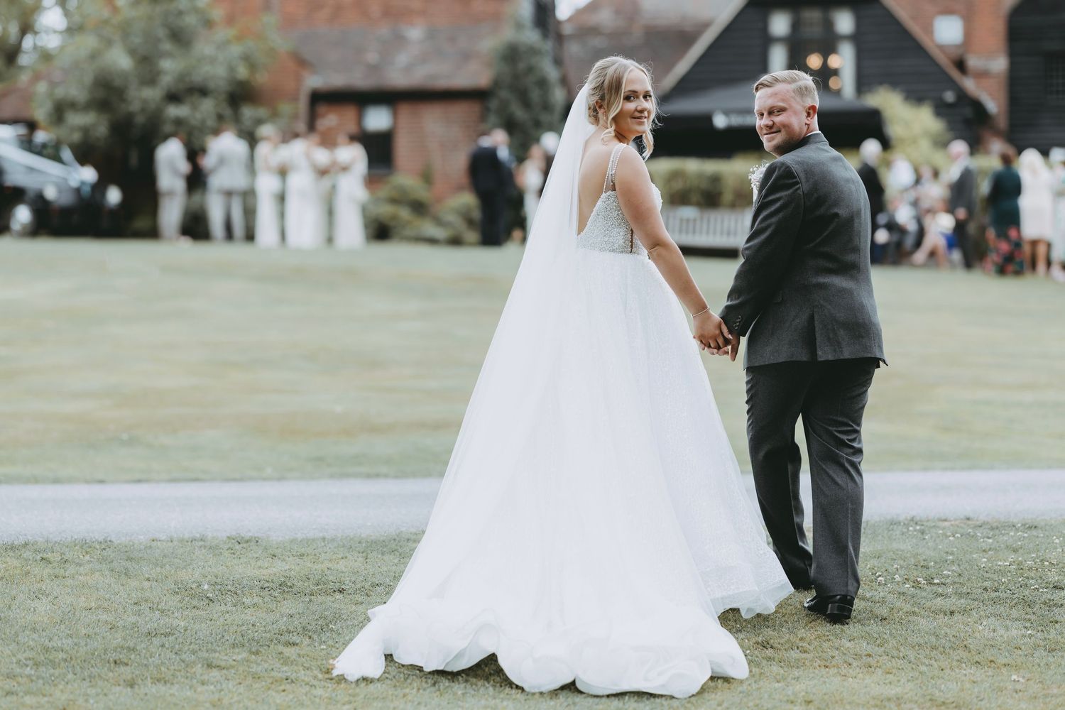Wide shot of wedding couple walking together across expansive lawn.