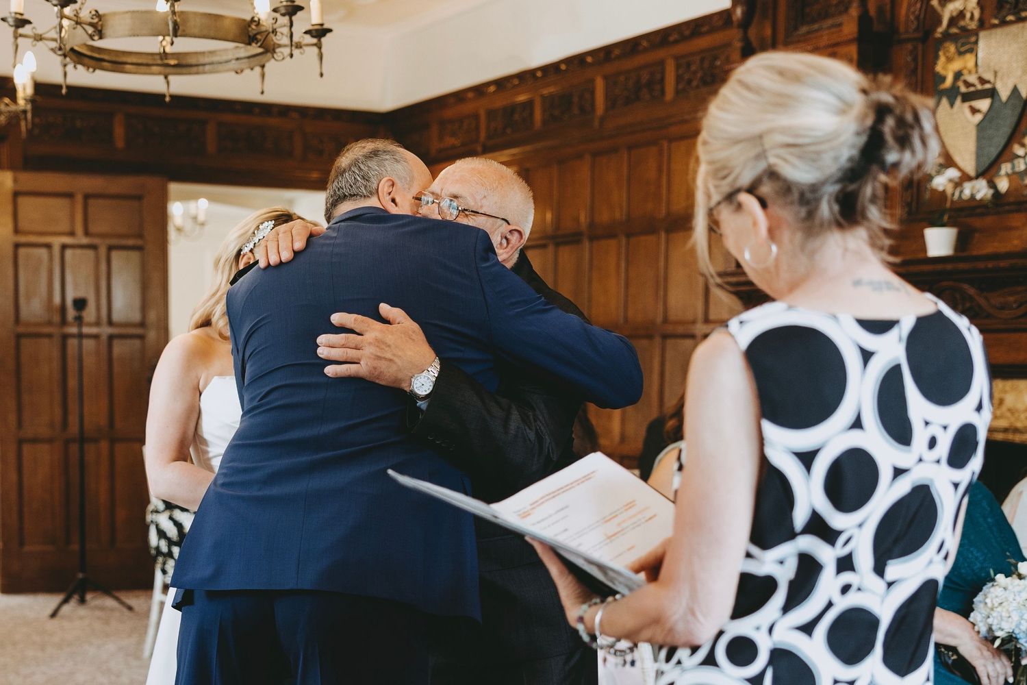 A touching embrace is shared during a wedding ceremony as an officiant holds a book.