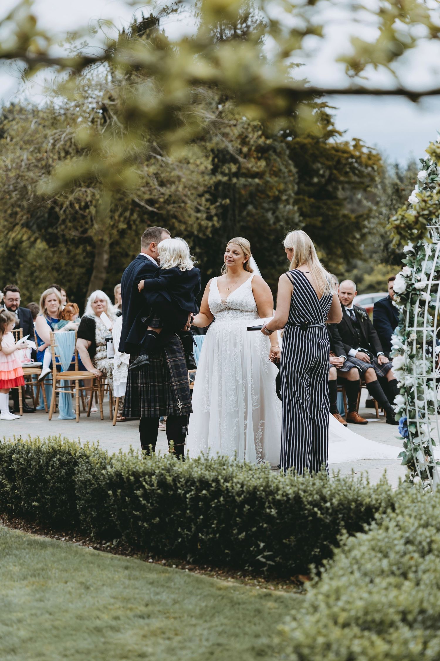 Garden wedding scene with guests mingling among decorative greenery and white floral arrangements.