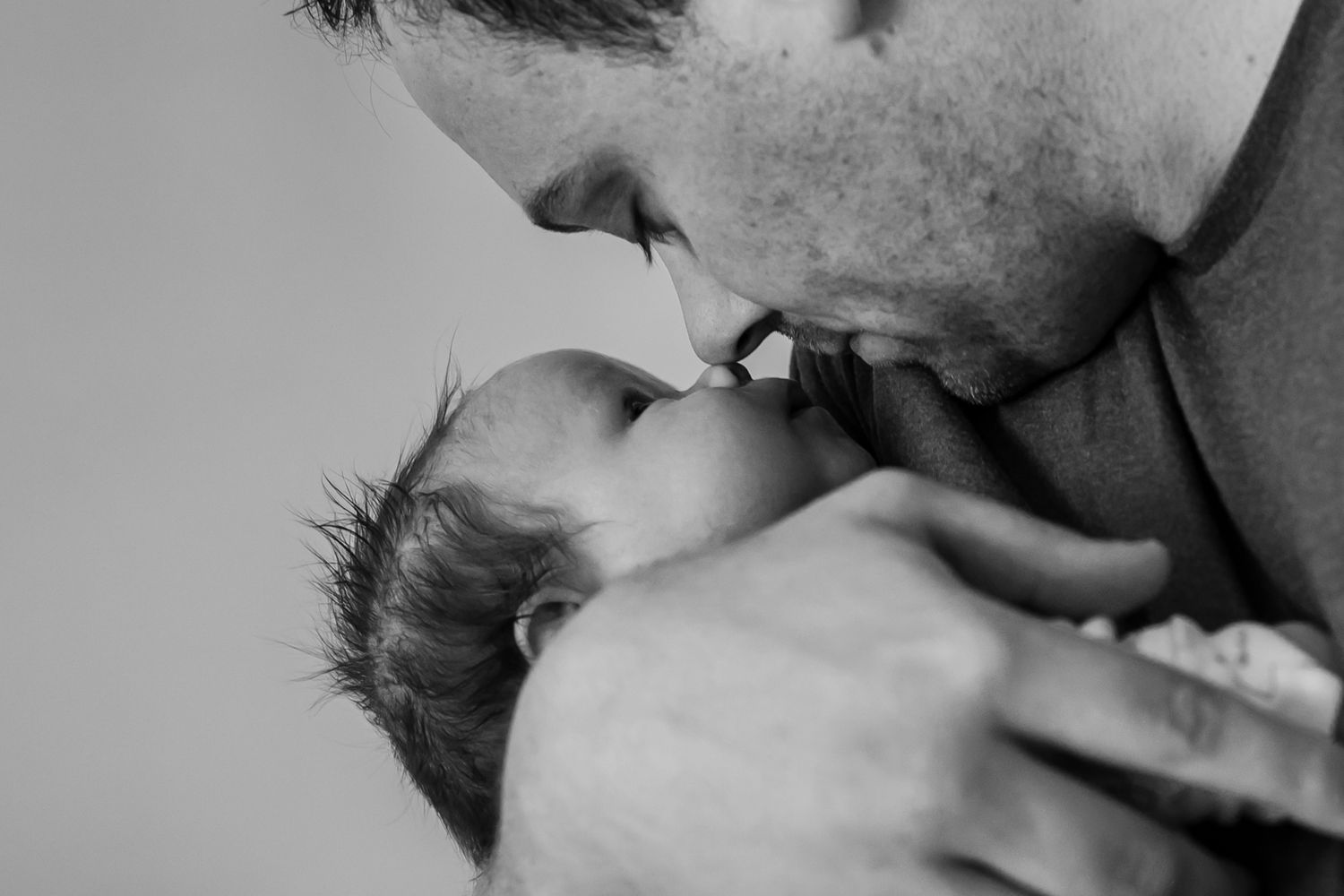 A tender black and white moment between parent and newborn baby captured in intimate close-up.