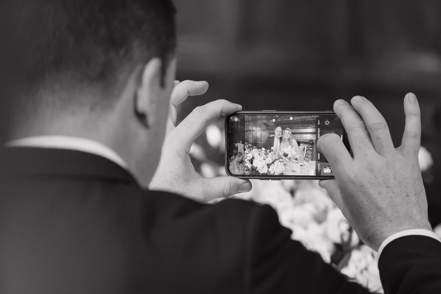 Black and white photo of guests taking pictures with phones at wedding reception.