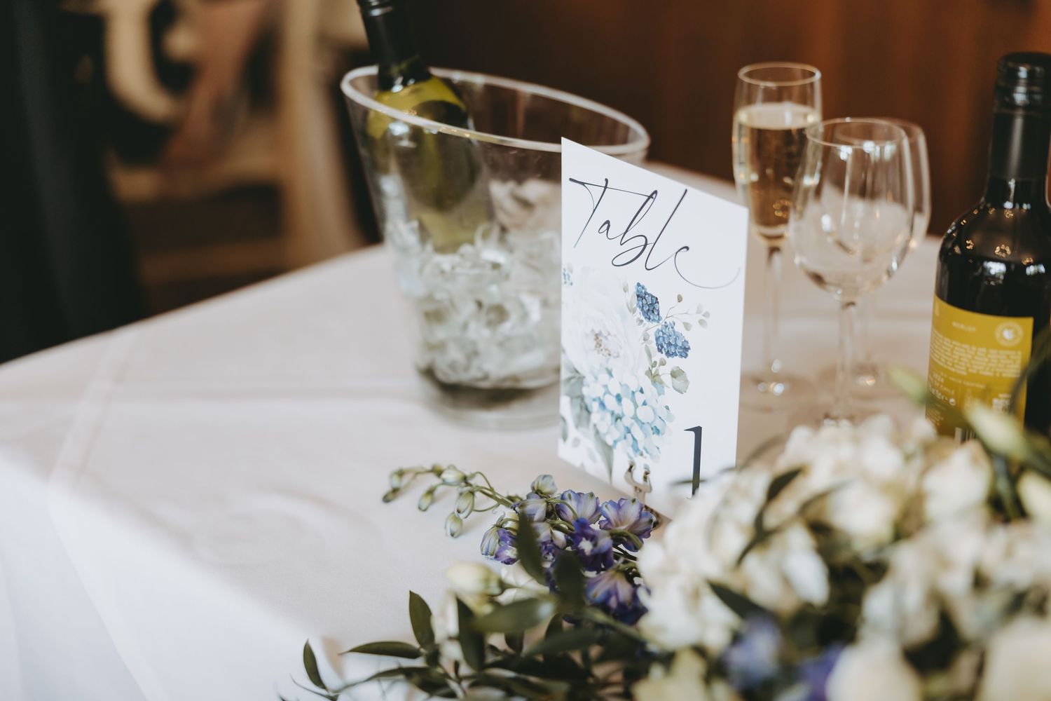 Wedding table setting with floral centerpiece and blue watercolor table number card.