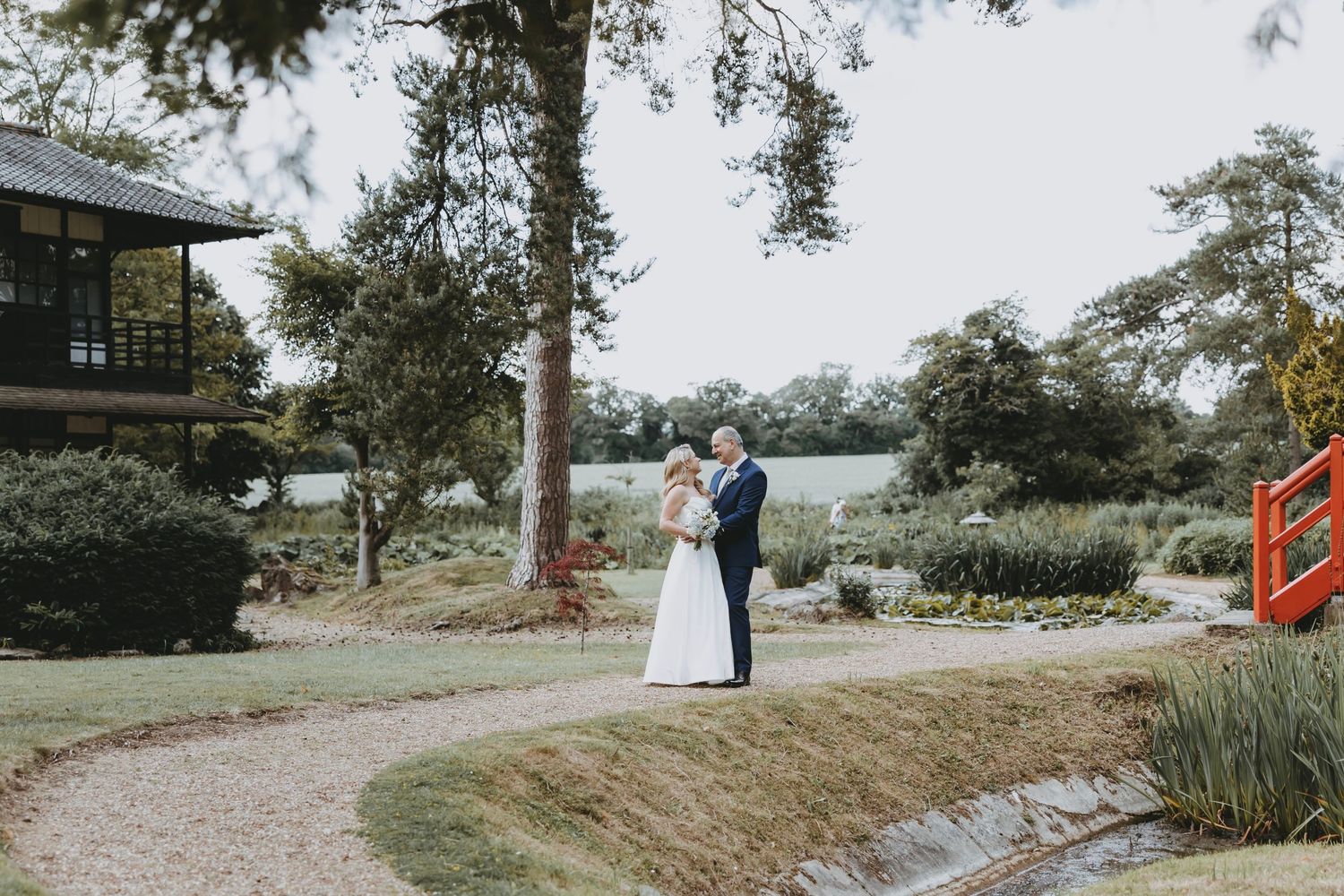 Wide landscape shots of a wedding couple in a scenic garden with pathways and trees at Fanham Hall, Ware, Hertfordshire.