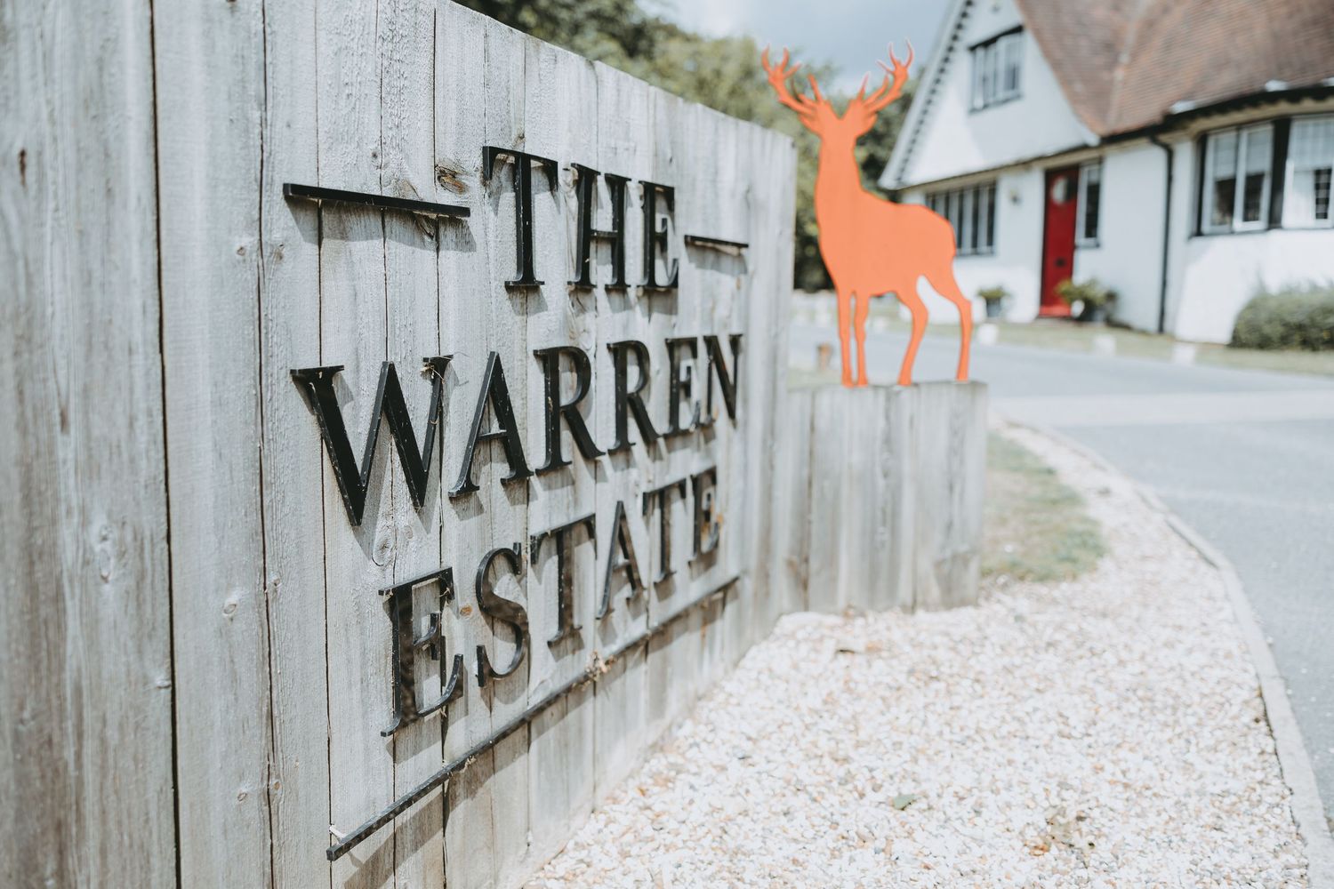 Wooden entrance sign for The Warren Estate with an orange decorative giraffe in background.