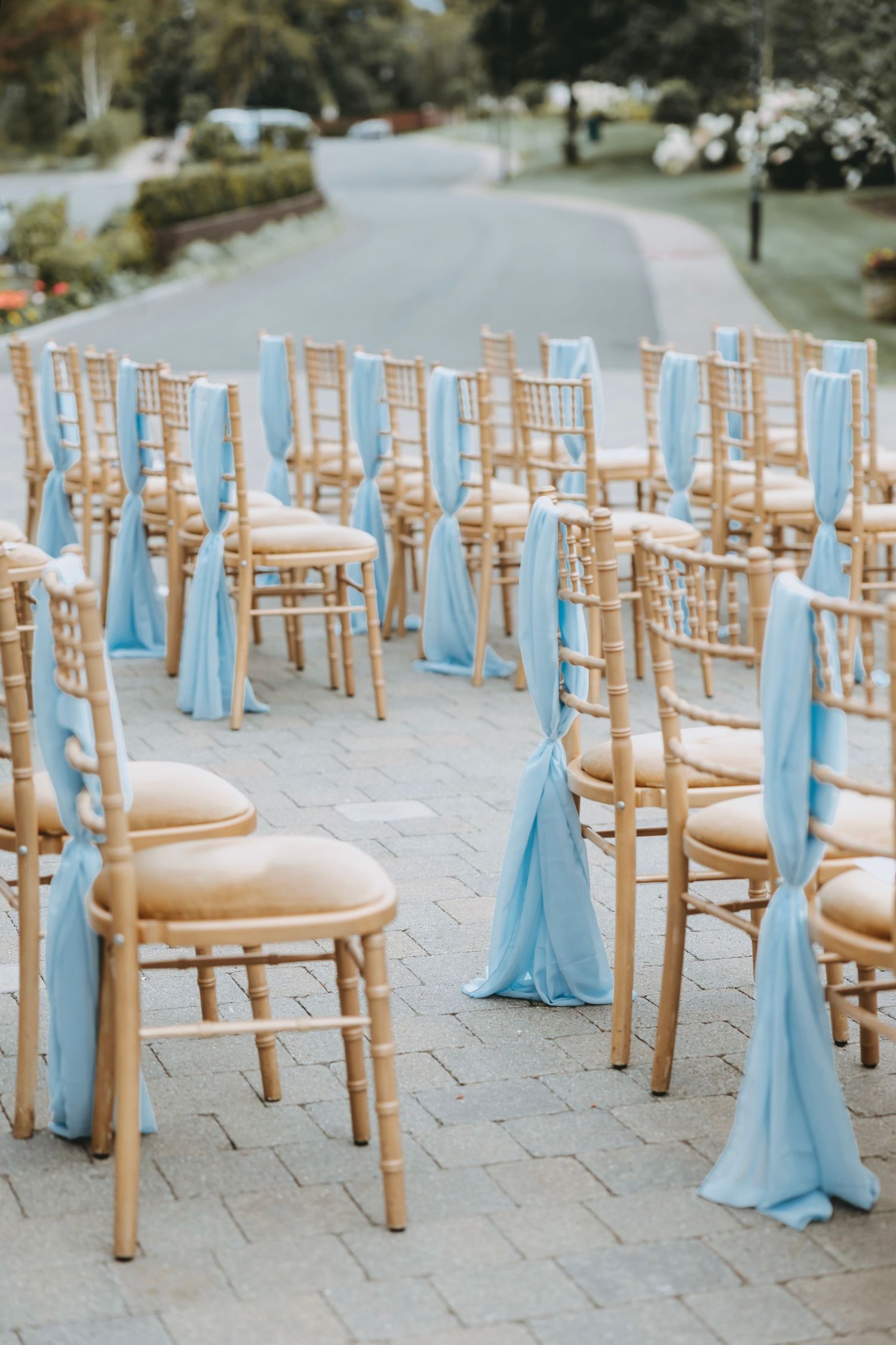 Wooden chiavari chairs with light blue sashes arranged for an outdoor wedding ceremony.