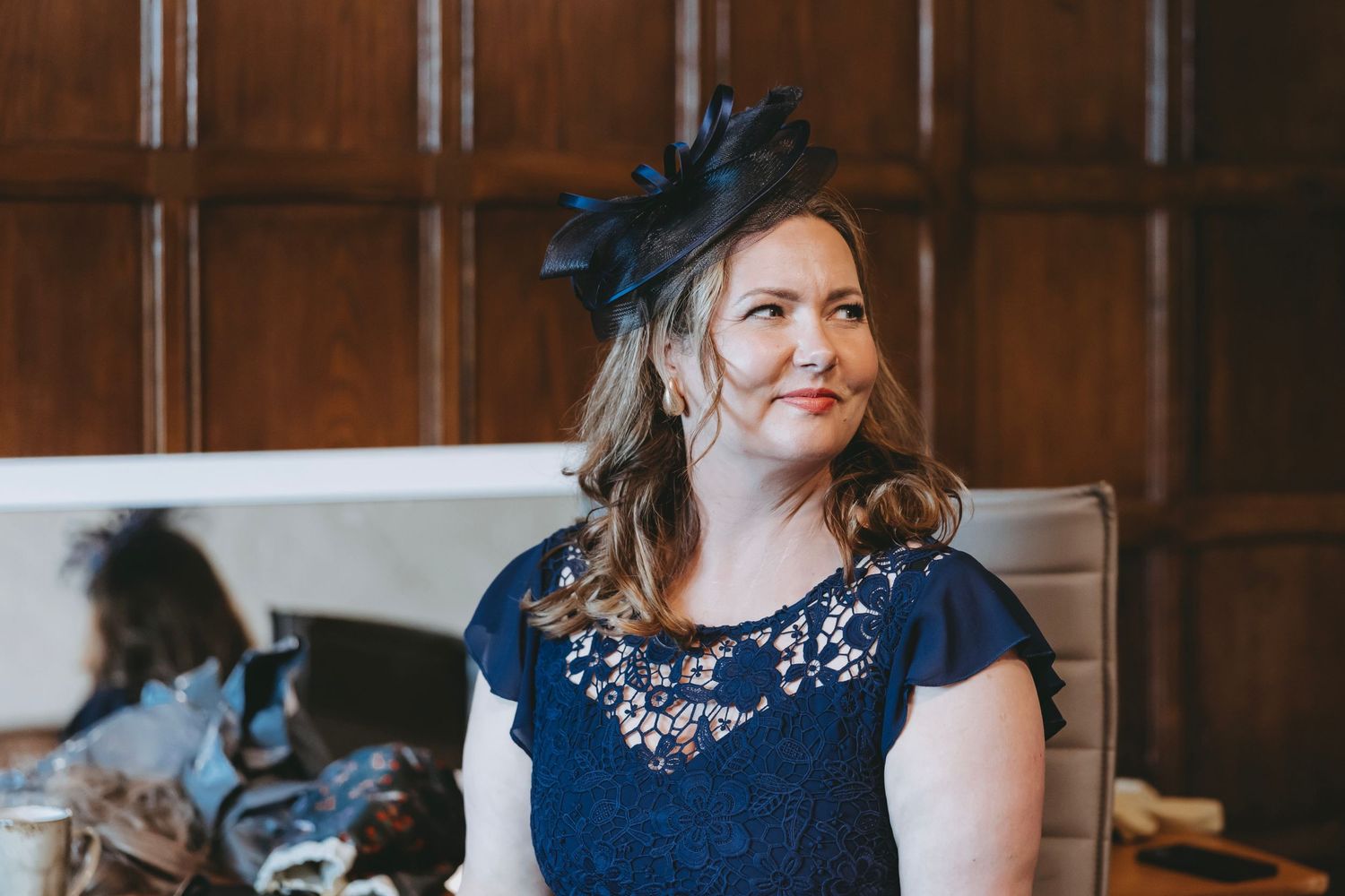 Woman wearing dark blue formal dress standing by window in classic interior.