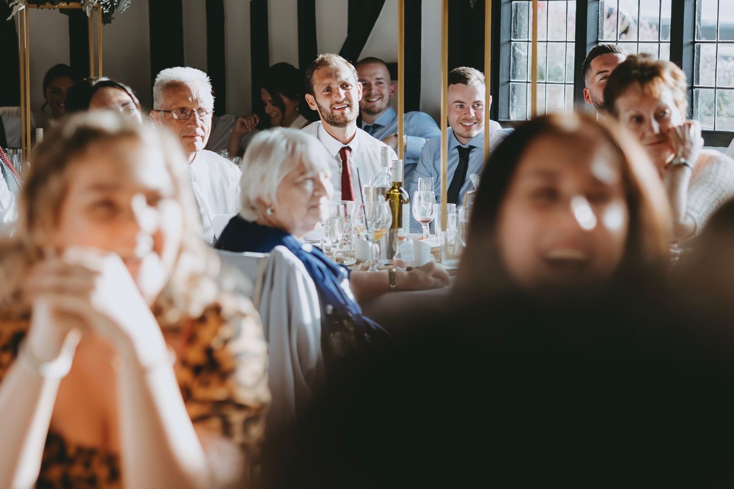 Wedding reception guests seated at long tables in a rustic venue with exposed wooden beams.