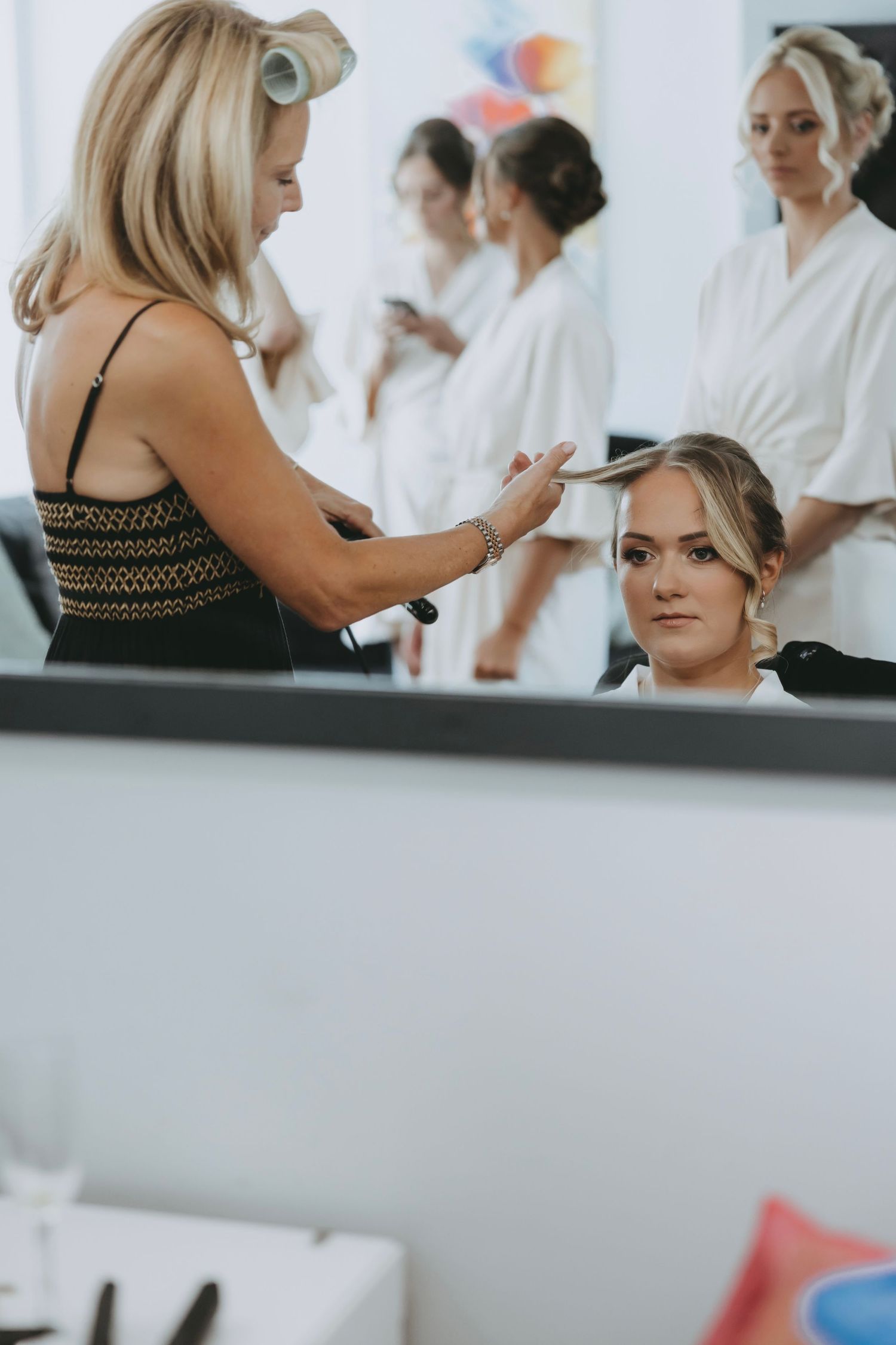 Wedding preparation scene with stylists working on hair in a bright indoor setting.