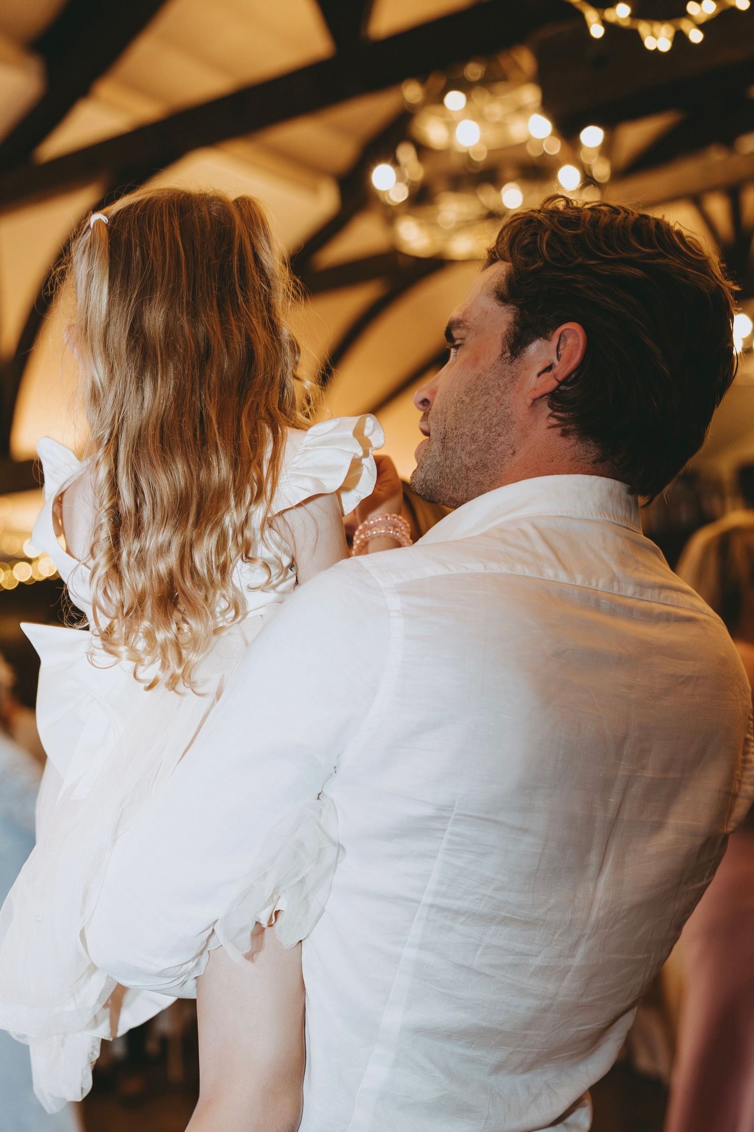 Wedding guests in white attire dance closely together under warm reception lighting.