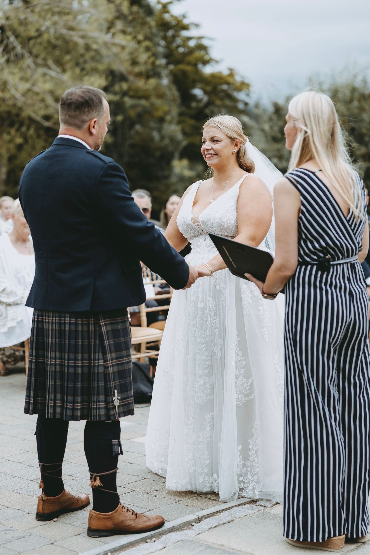 Wedding guests in formal wear and kilts socialize during an outdoor reception.
