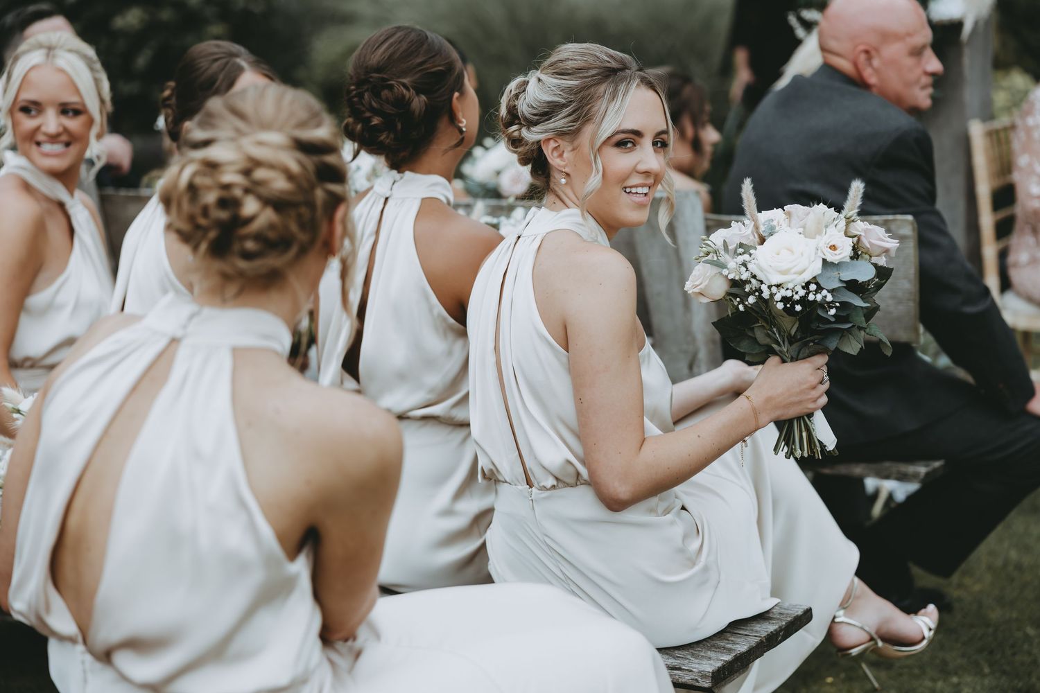 Bridesmaids in elegant white dresses gather during outdoor wedding celebration.