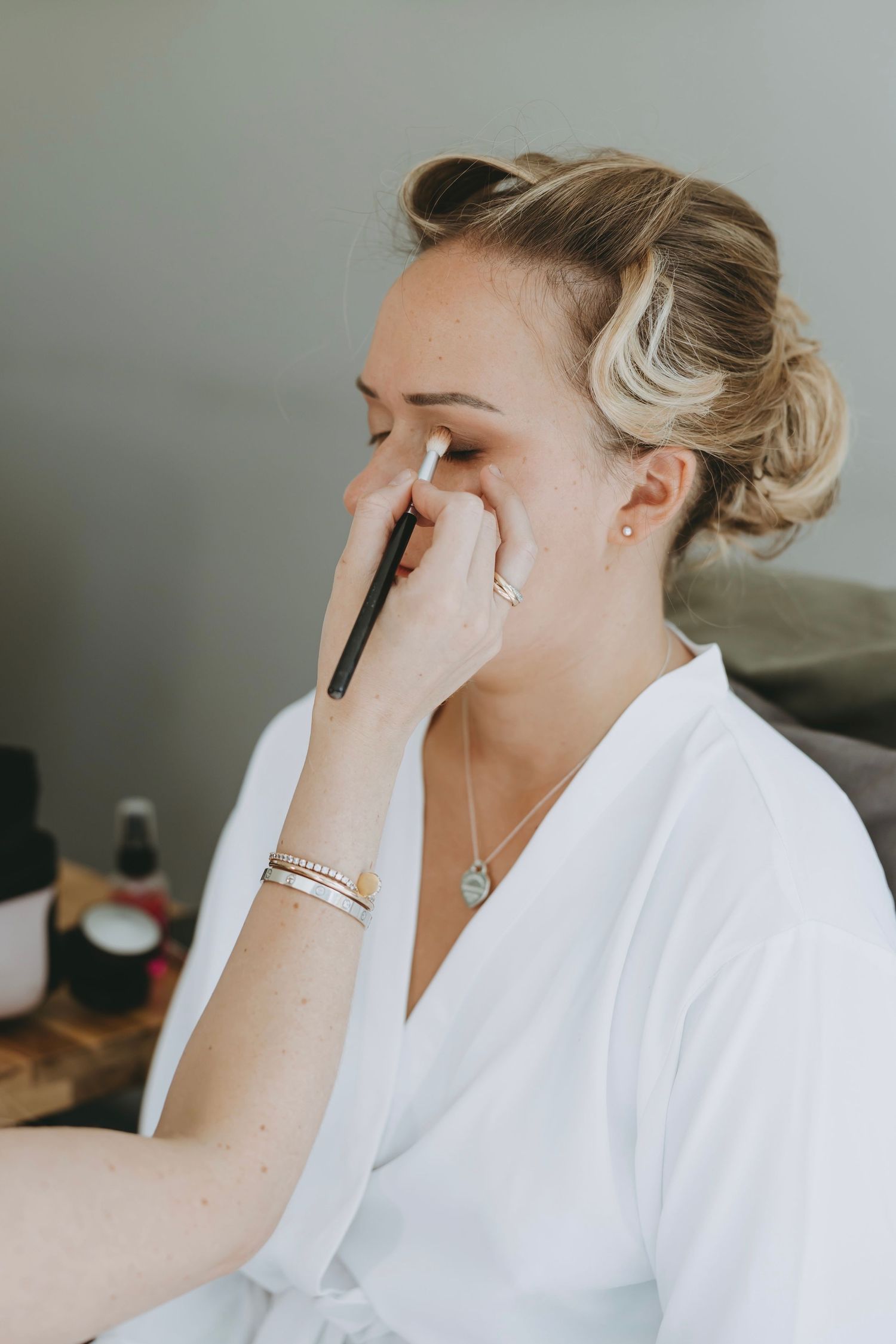Makeup artist applying cosmetics to someone wearing a white bathrobe during bridal preparations.