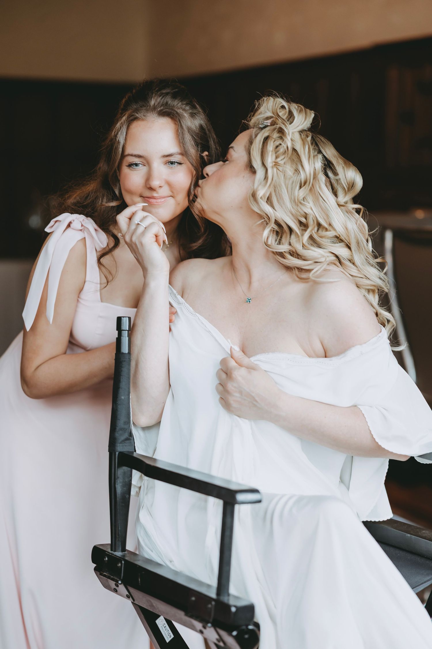 Women in white dresses share joyful moments during wedding preparations.