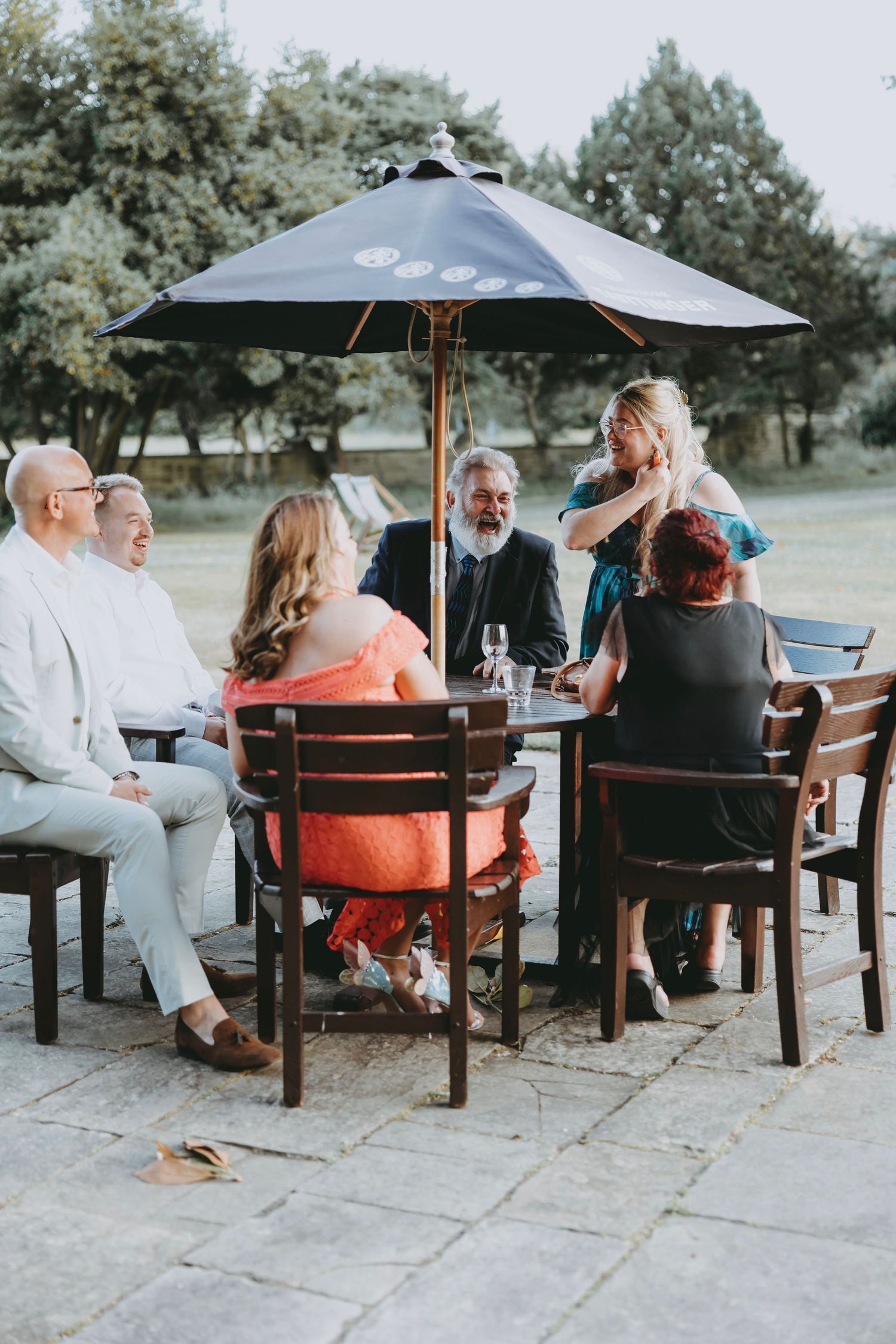 People gathered under patio umbrellas at wooden tables for an outdoor social event.