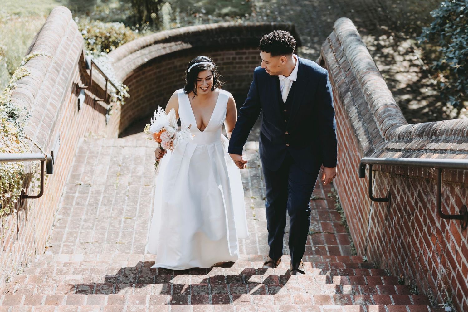 A couple walks up brick steps together on their wedding day.