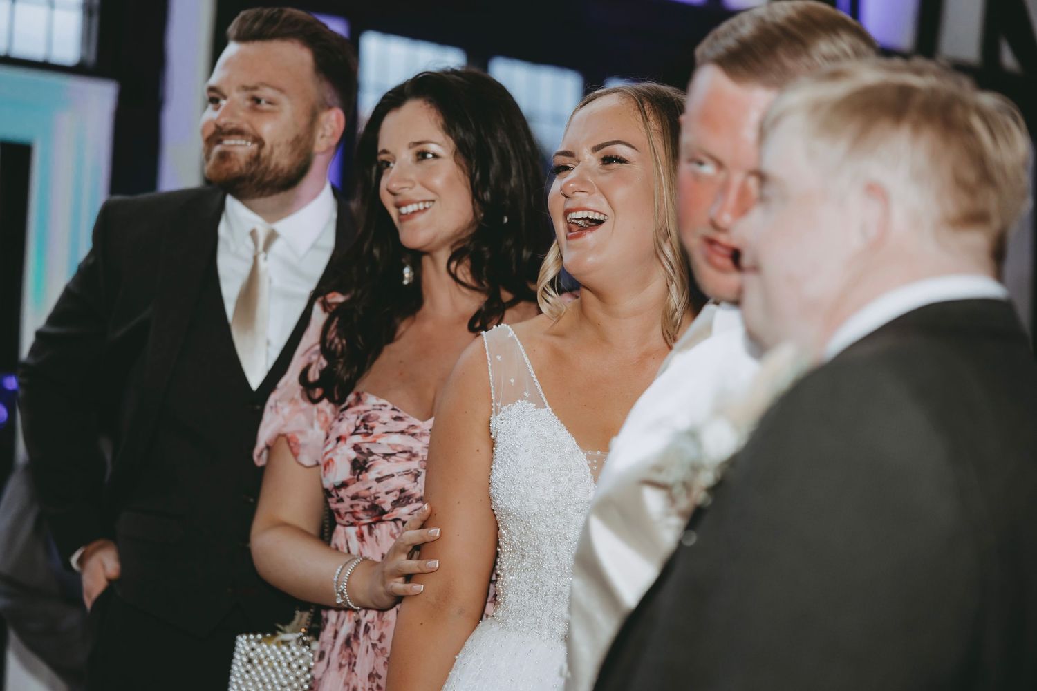 Wedding party members and guests sharing laughter during indoor reception celebration.