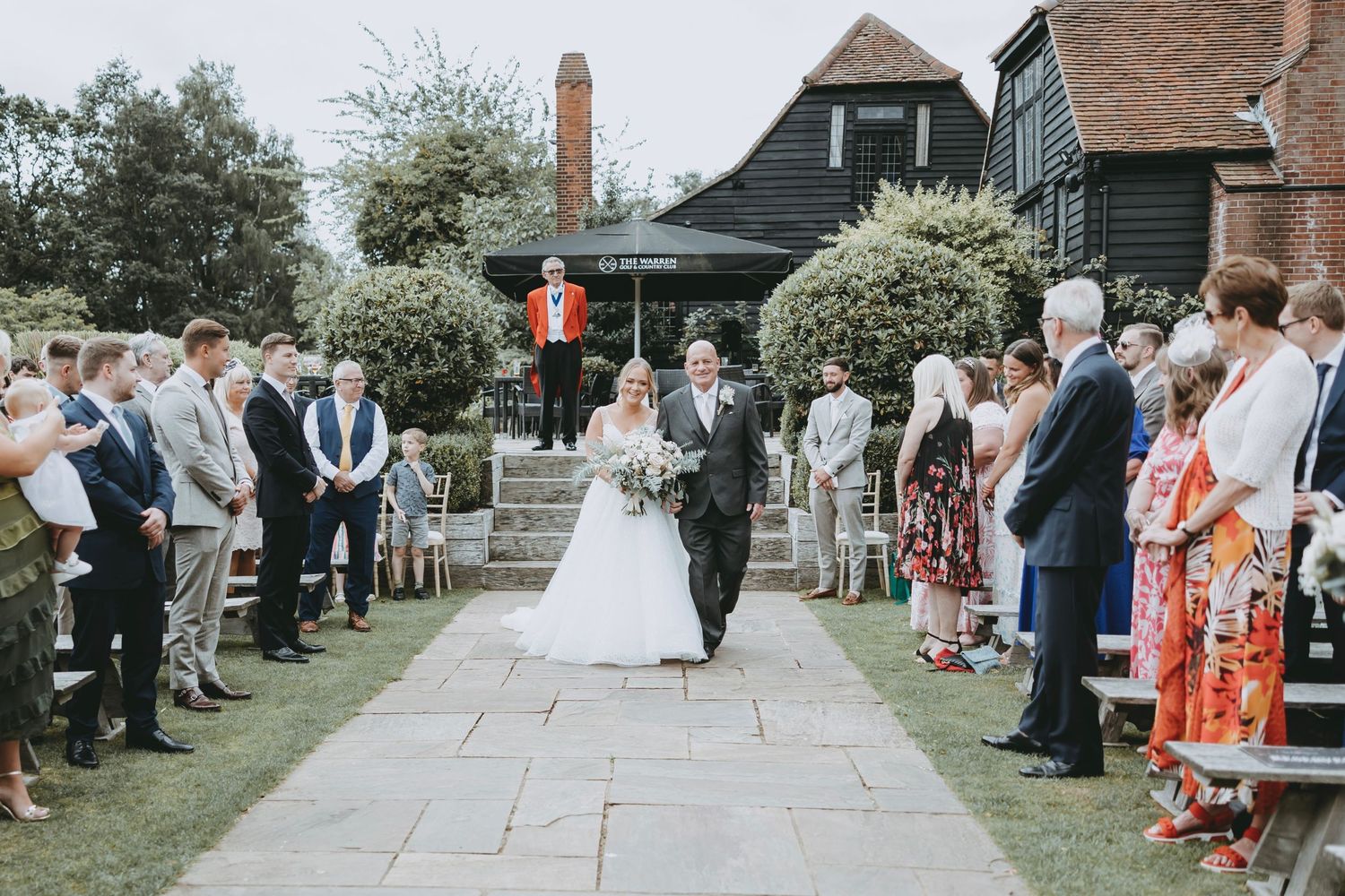 Wedding ceremony procession along stone pathway with guests lined up on both sides.
