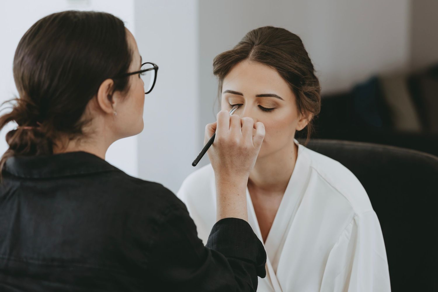 Beauty preparation scene with women in white robes in natural light setting.
