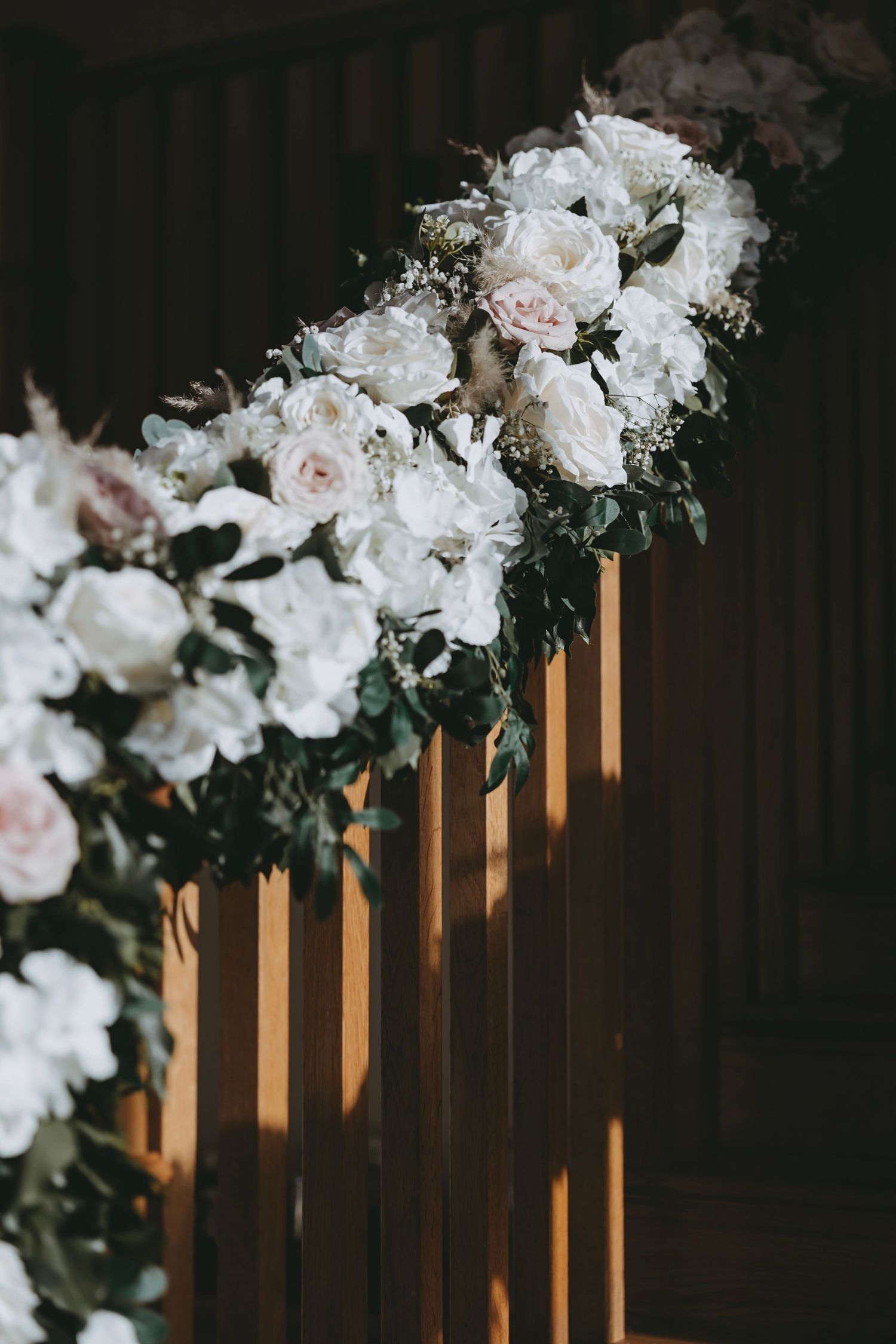 Elegant white floral arrangements adorning wooden pillars at a wedding venue.