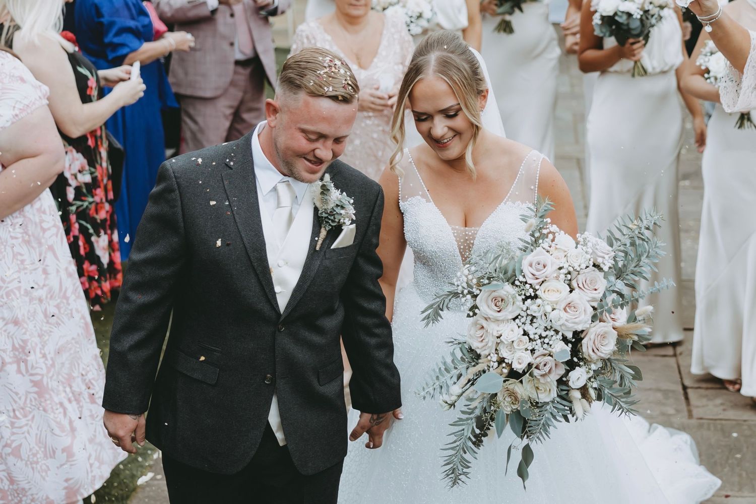 Wedding party walks through shower of confetti during outdoor celebration.