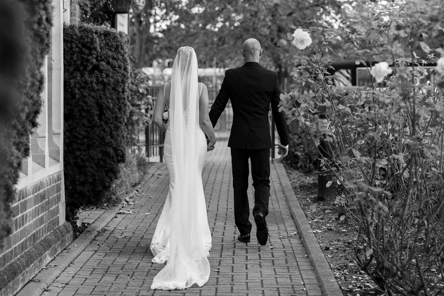A sequence of black and white photos showing a couple walking along a brick path surrounded by greenery.