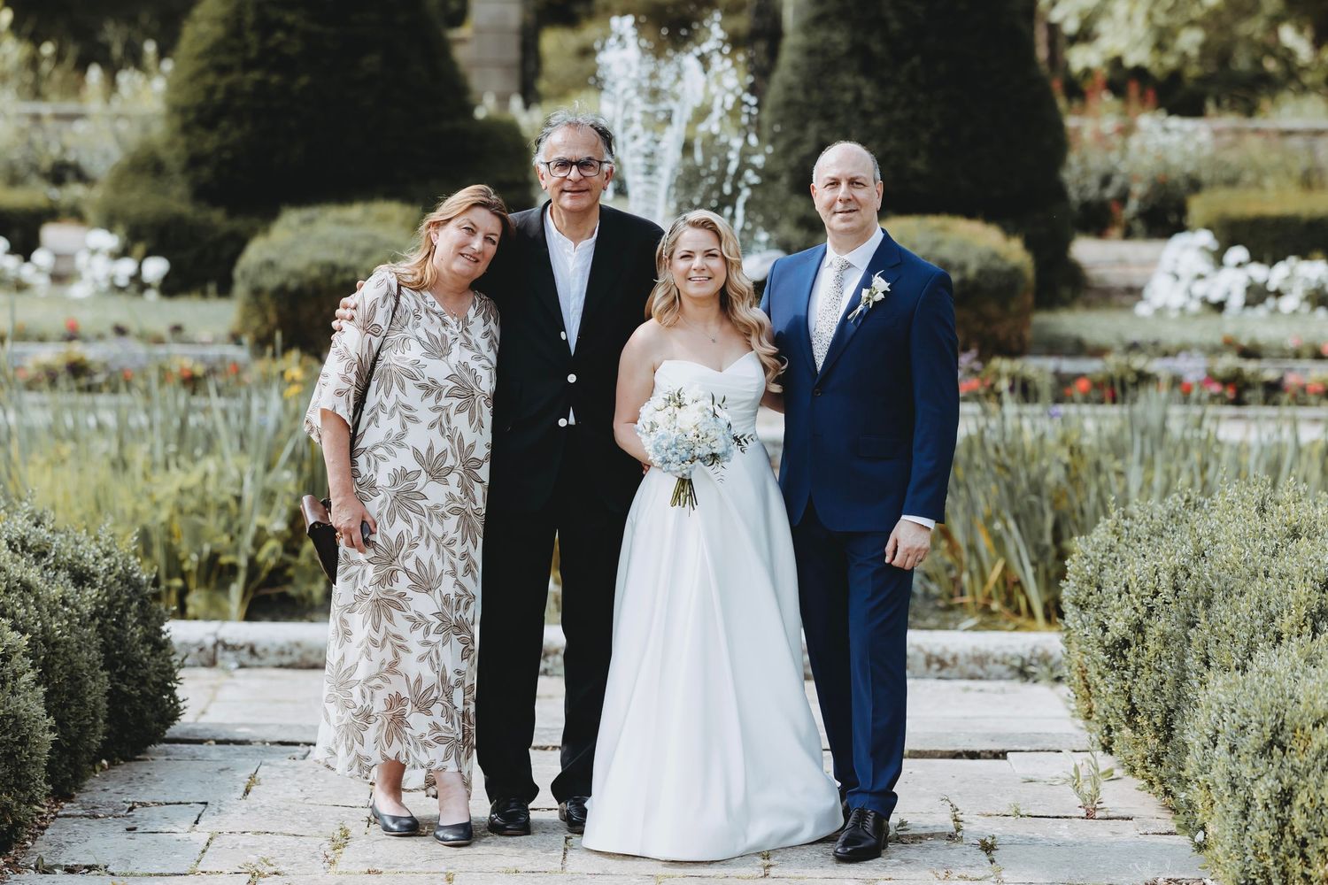 Wedding celebration group poses for formal photos in landscaped garden setting.