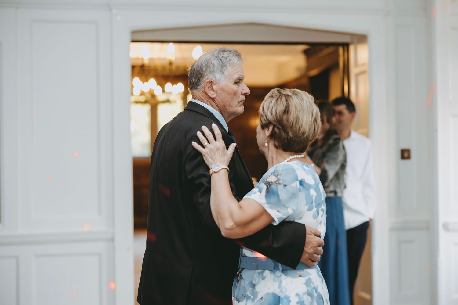 Two people share a tender dance moment at an elegant indoor venue with warm lighting in the background.