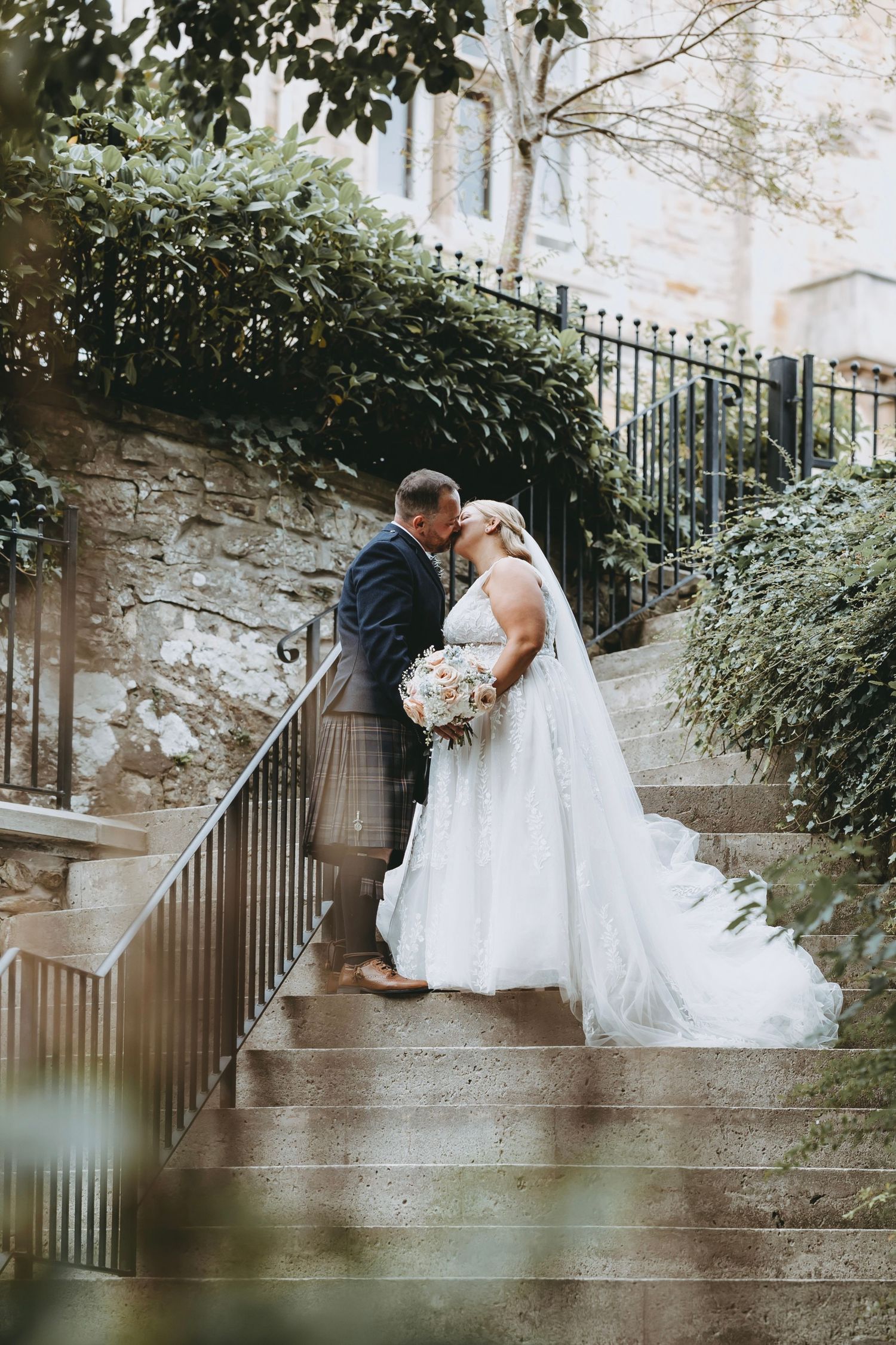 Wedding couple sharing intimate moments on rustic stone steps with wrought iron railing and lush greenery.