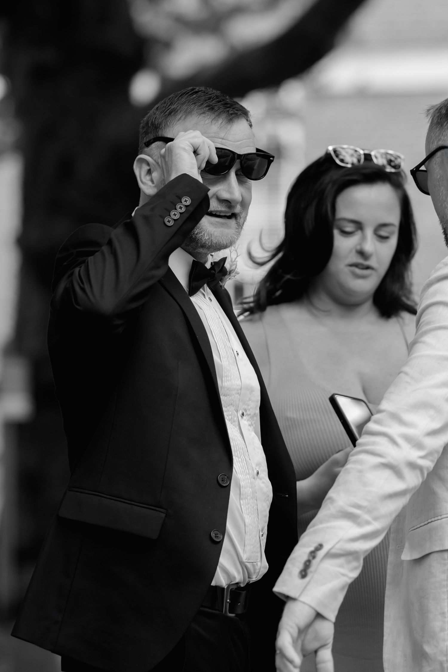 A black and white candid photo of wedding guests in formal attire.
