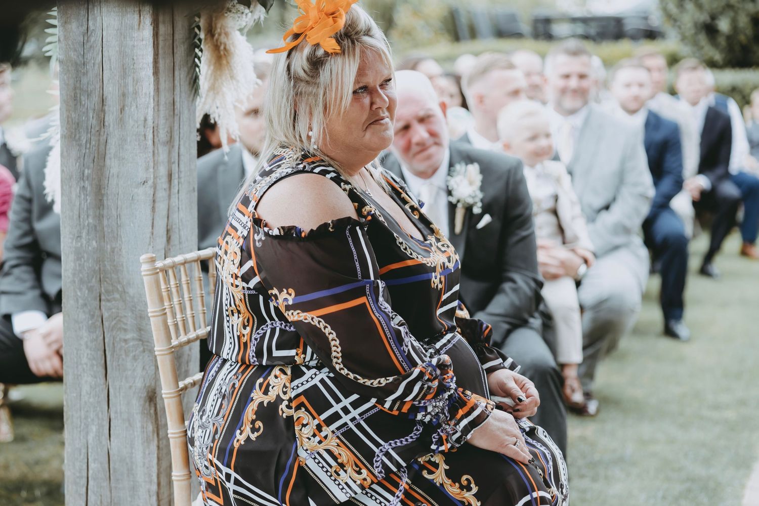 Guest in patterned dress seated at outdoor wedding ceremony.