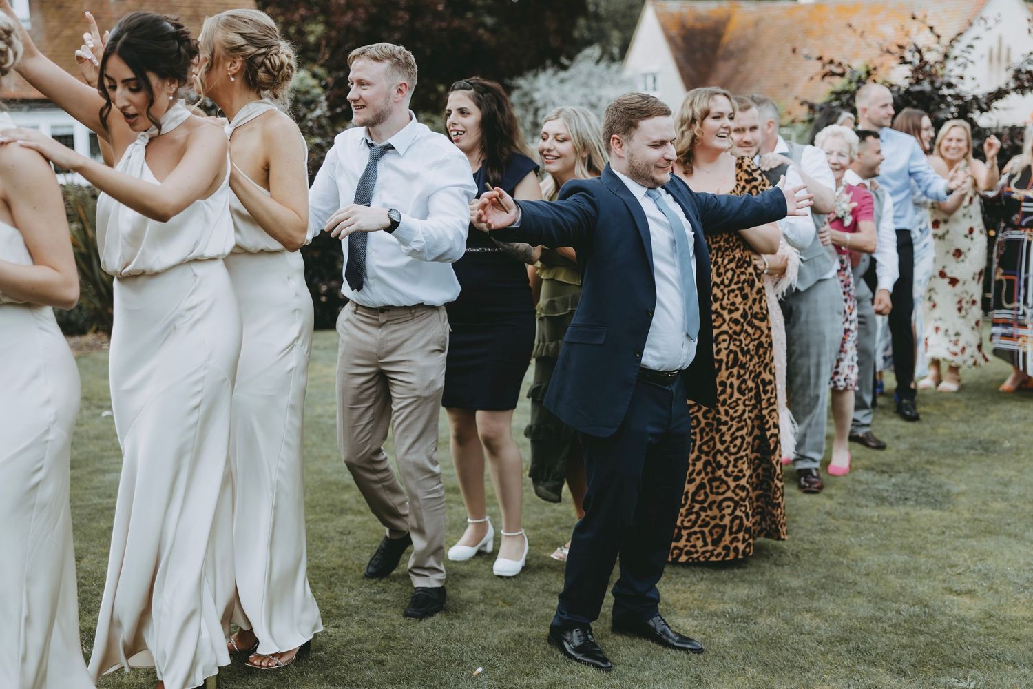 Wedding guests in formal attire gather on a lawn during a summer celebration.