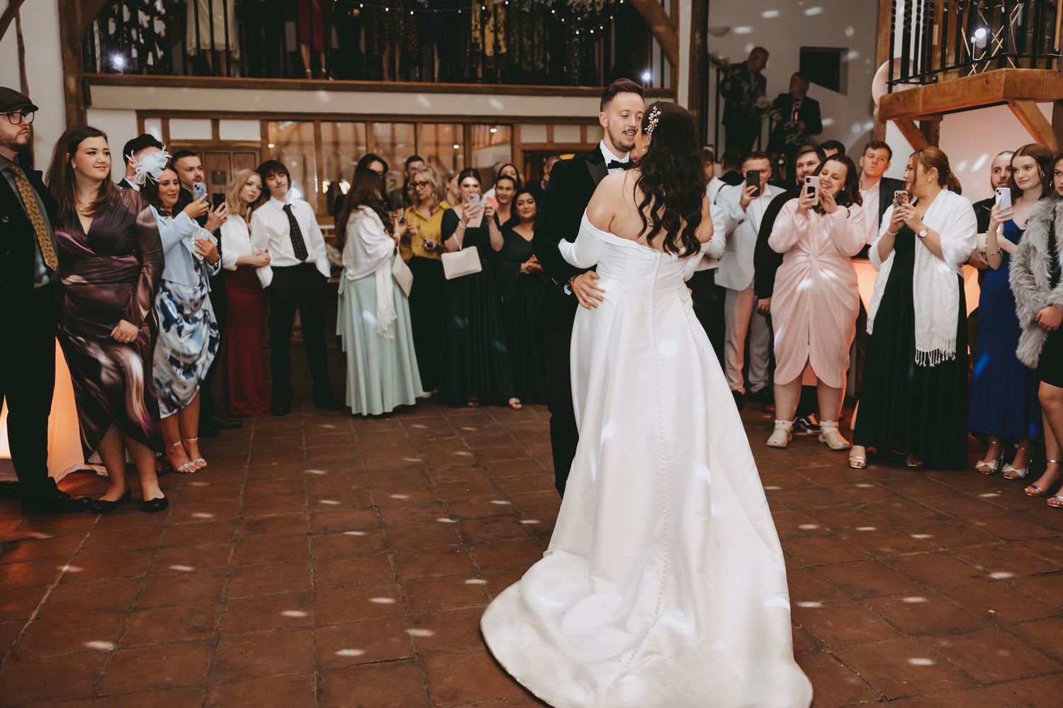 A couple shares their first dance at a wedding reception while guests watch from the dance floor perimeter.