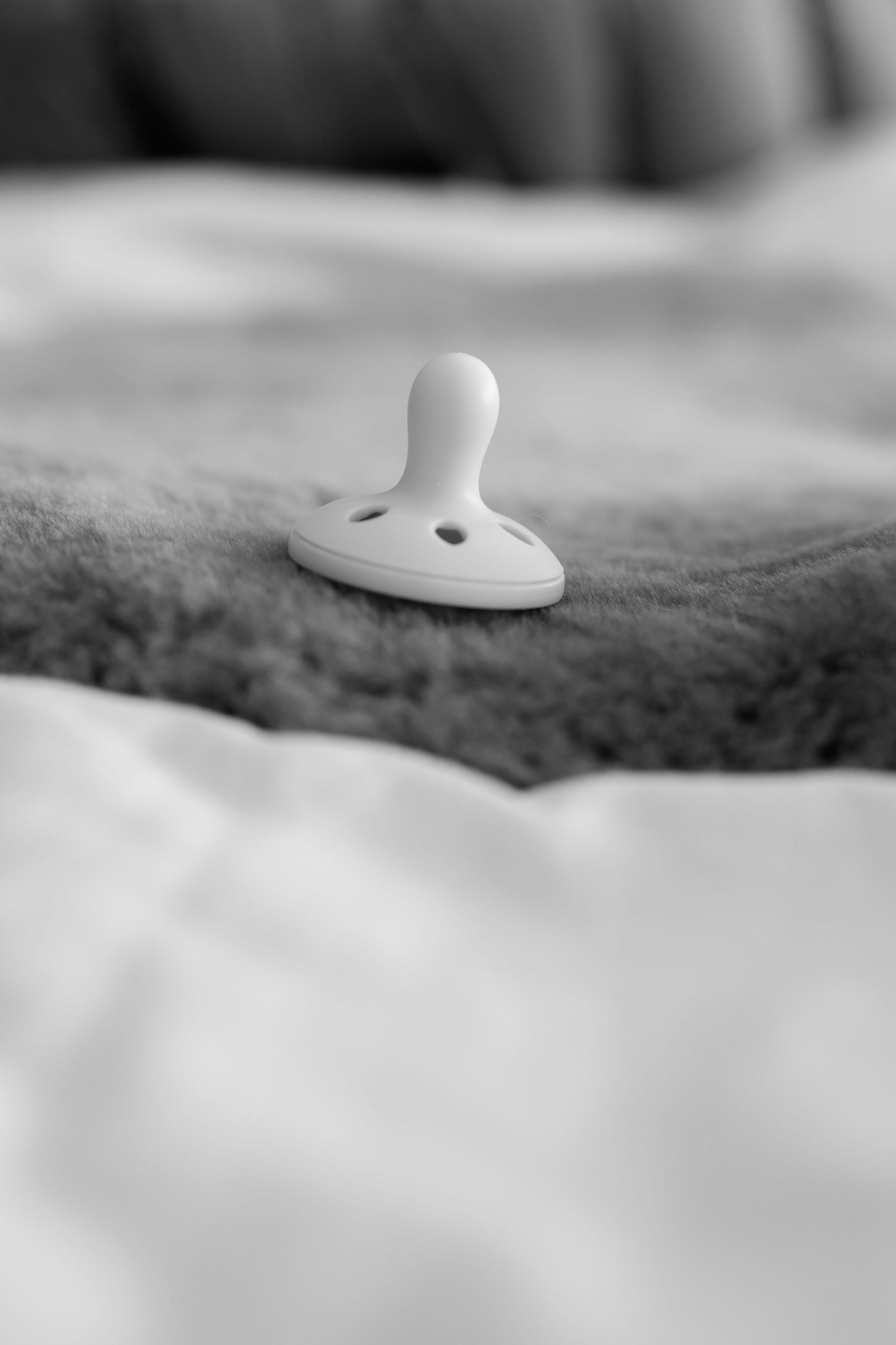 A white pacifier rests on soft fabric in black and white macro photography.