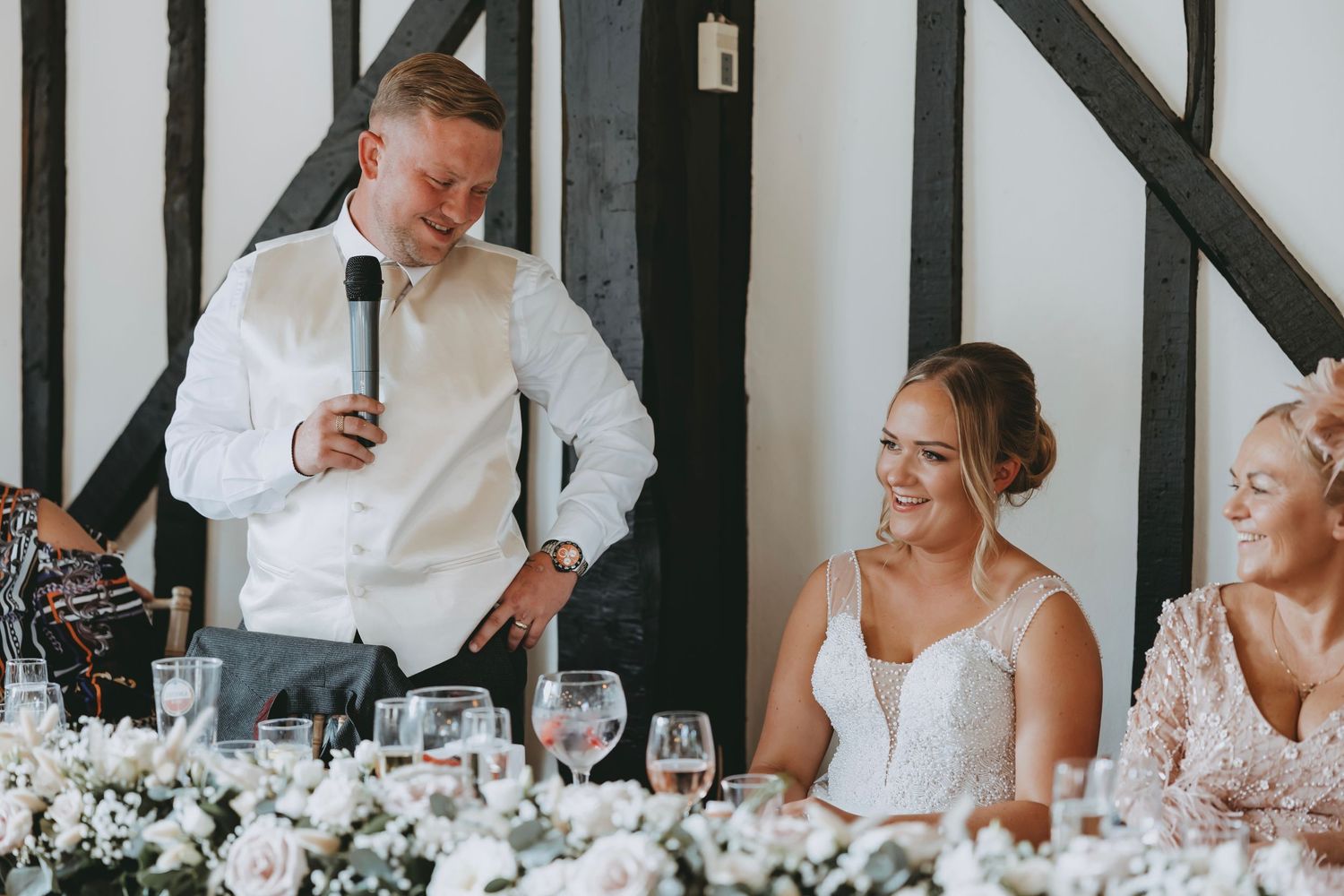 Wedding reception venue decorated with white floral arrangements and exposed wooden beams.