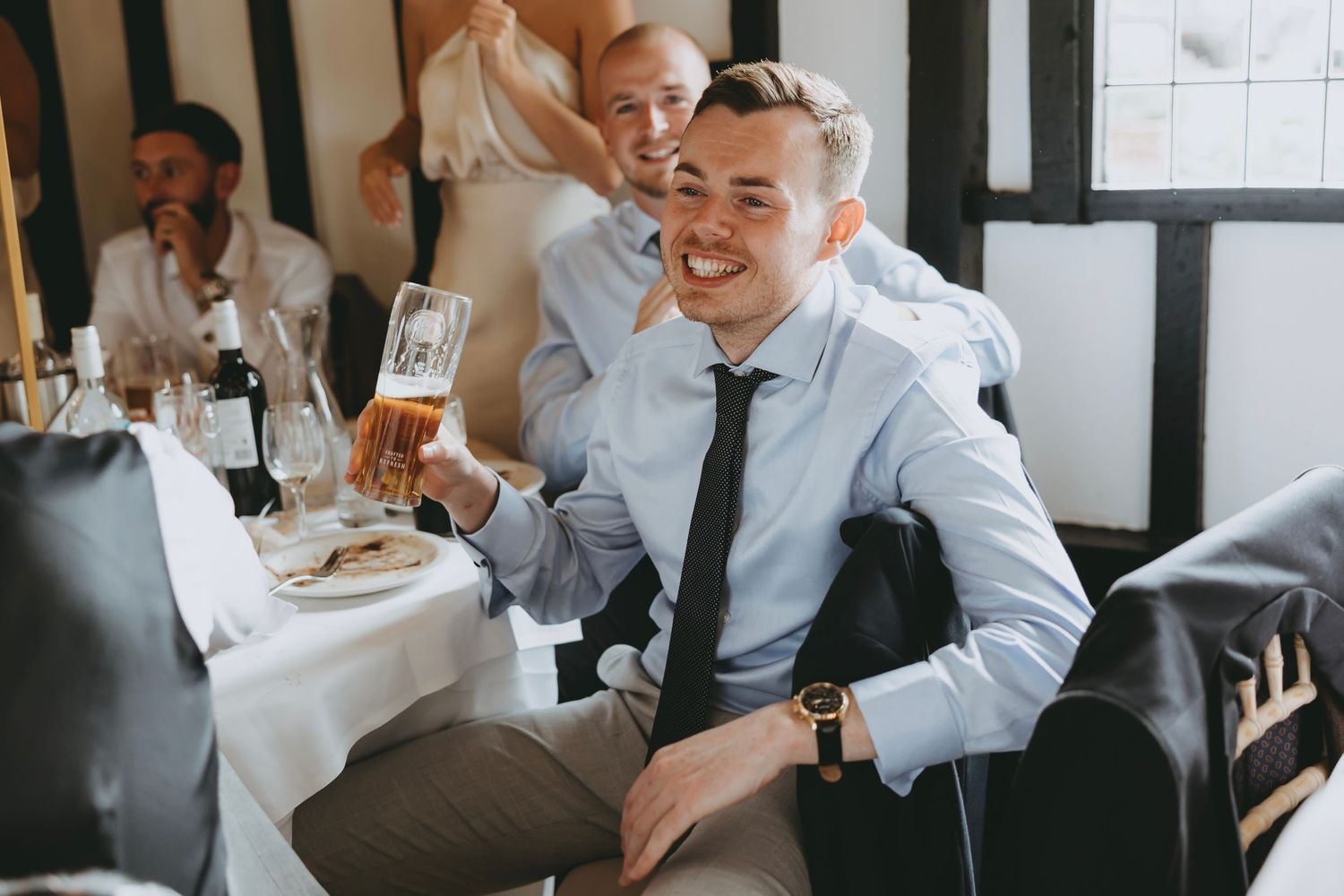 Guests laugh and celebrate at an indoor wedding reception with white decor.