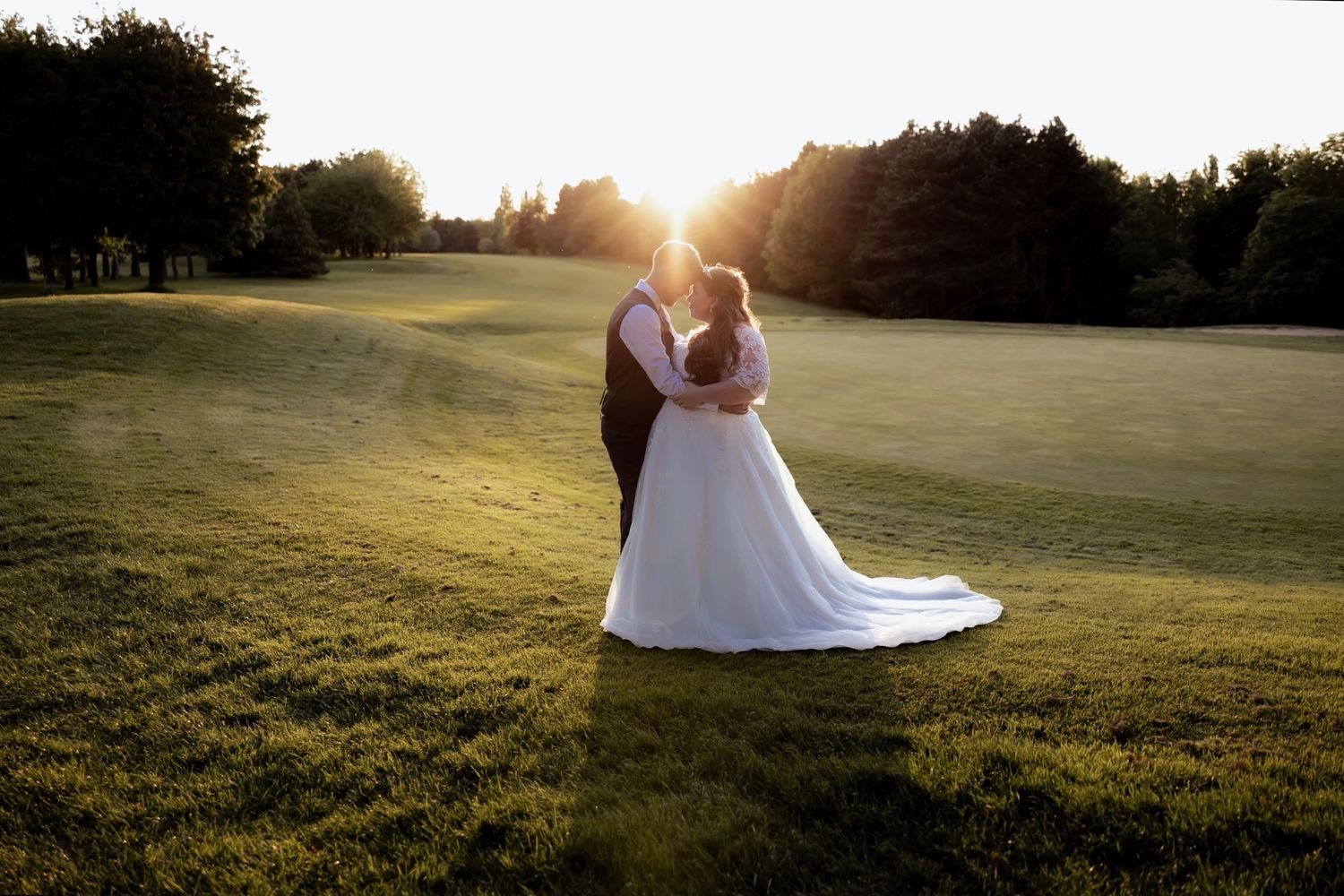Golden sunset illuminates wedding couple in grassy field during outdoor photo session.