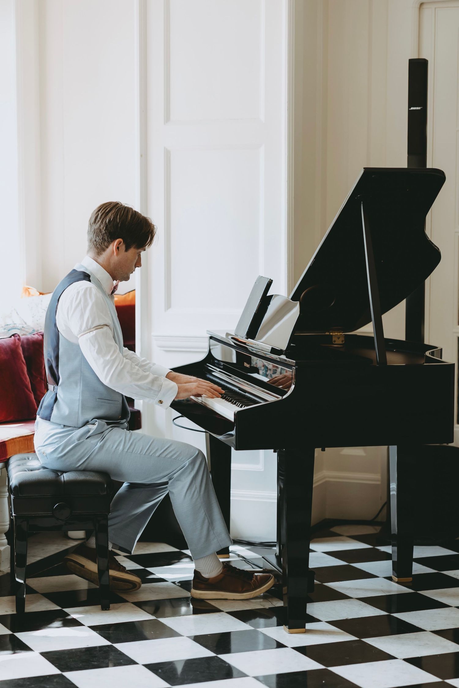 Pianist in light gray suit performing on grand piano on checkered floor.
