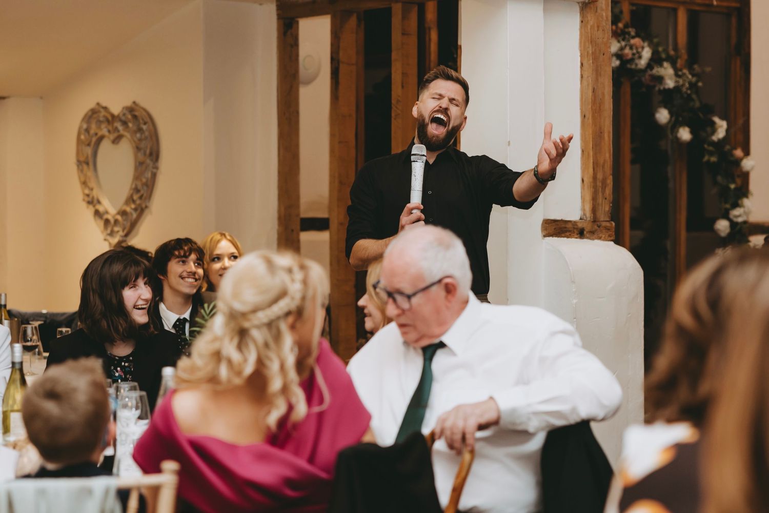 Wedding reception guests dancing and celebrating in a rustic venue with wooden beams.