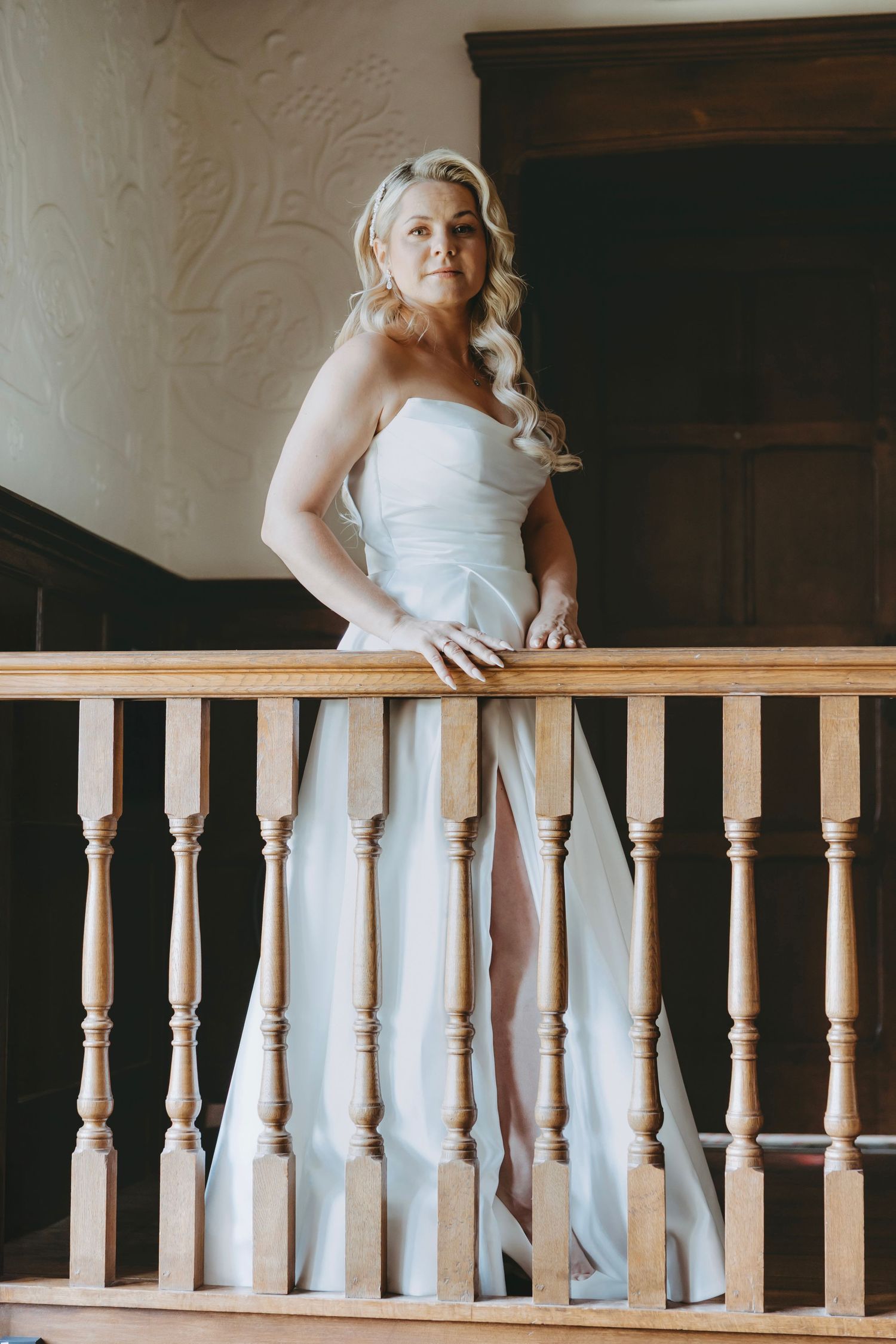Person in white dress poses against wooden railing in vintage-style interior.