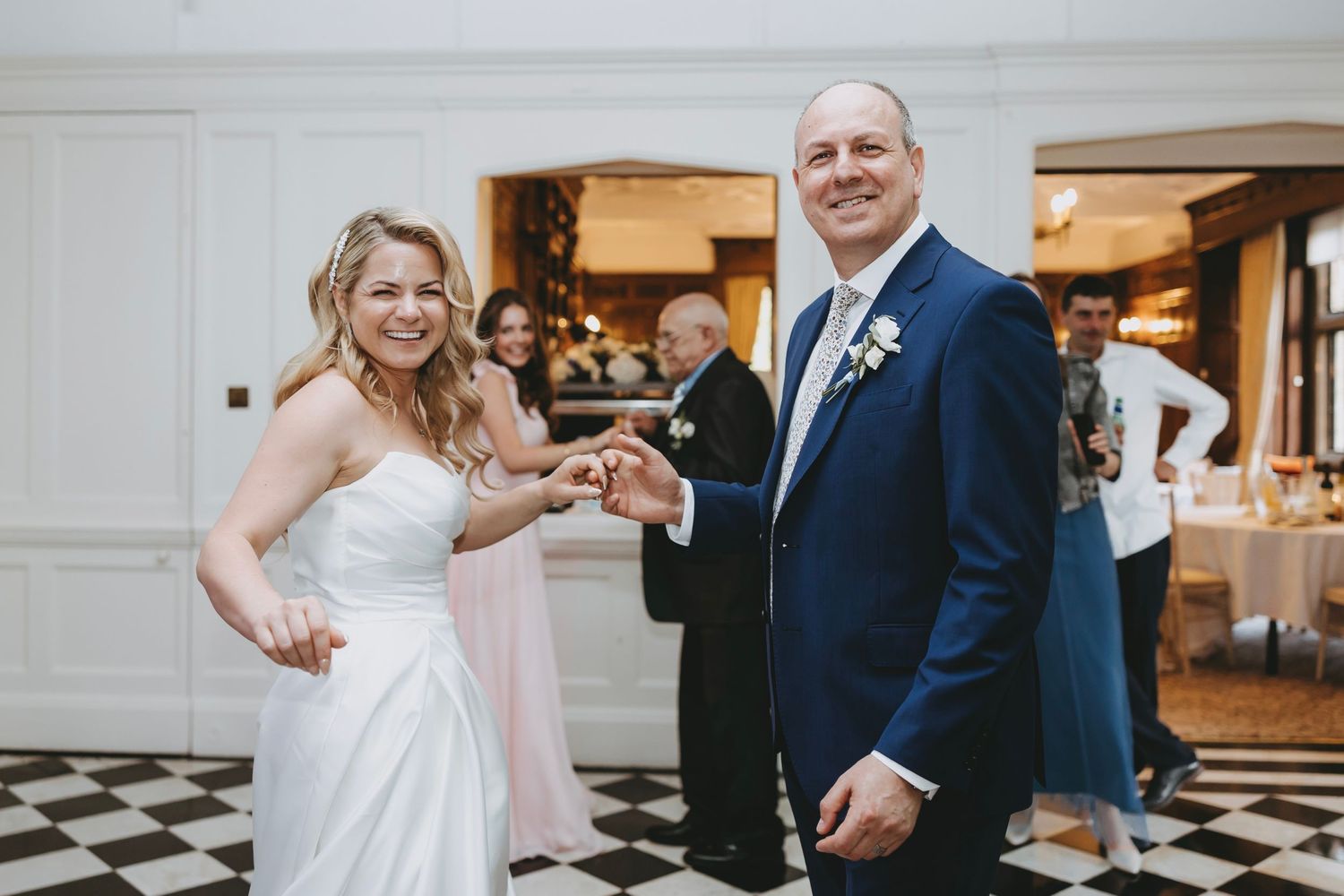 Wedding party members dance and celebrate in a brightly lit reception hall.