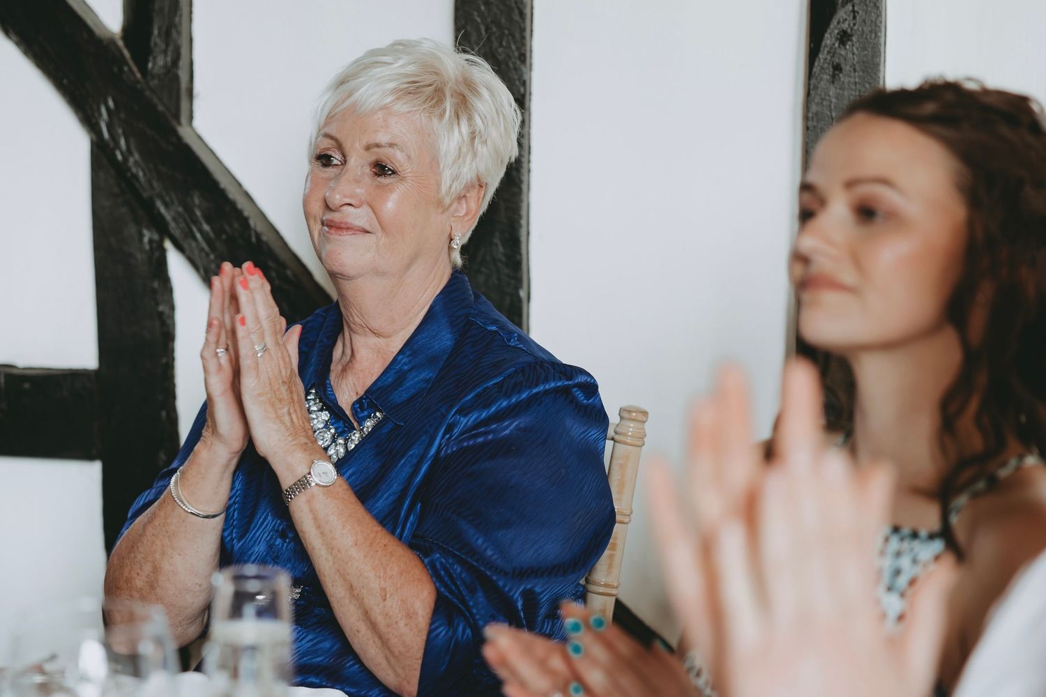 Wedding guests react with laughter and joy during speeches at an indoor reception venue.