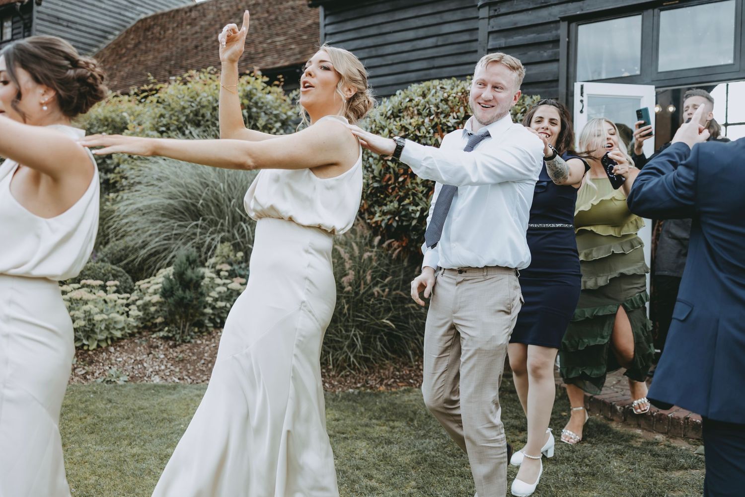 Wedding party members dancing outdoors in casual summer attire.