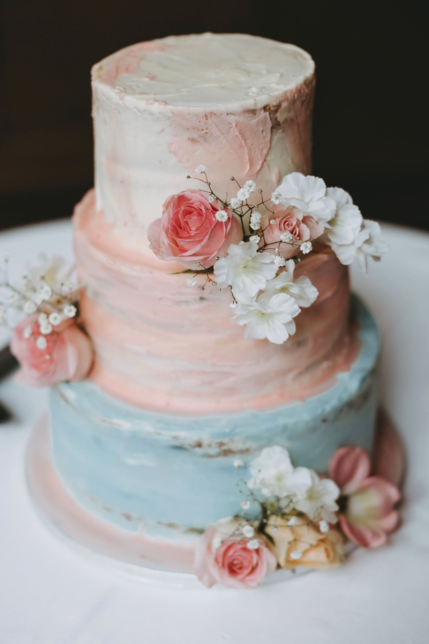 Close-up of a pink and blue wedding cake adorned with fresh roses and white floral decorations.