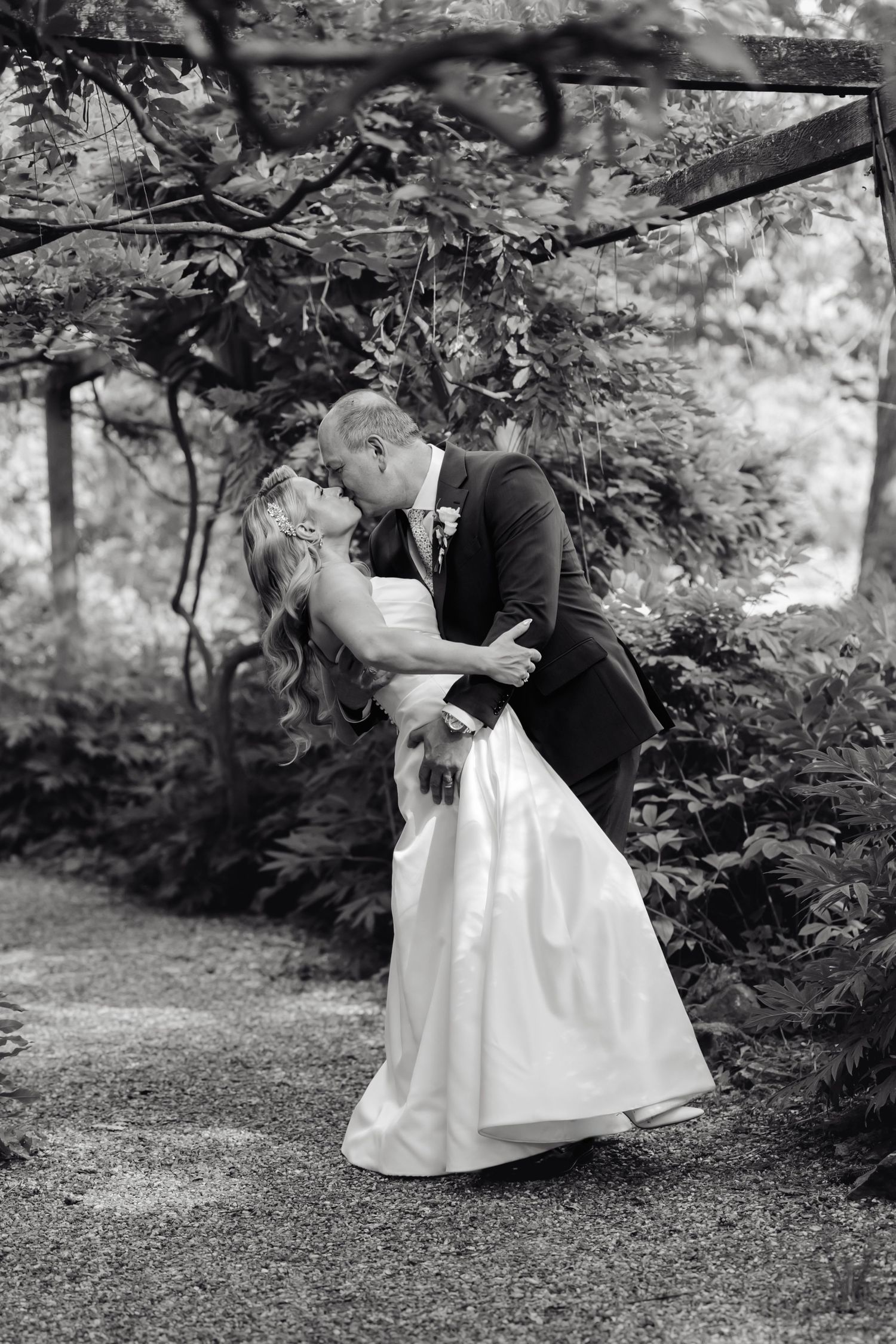Romantic black and white wedding portrait in garden setting with dramatic dip pose.