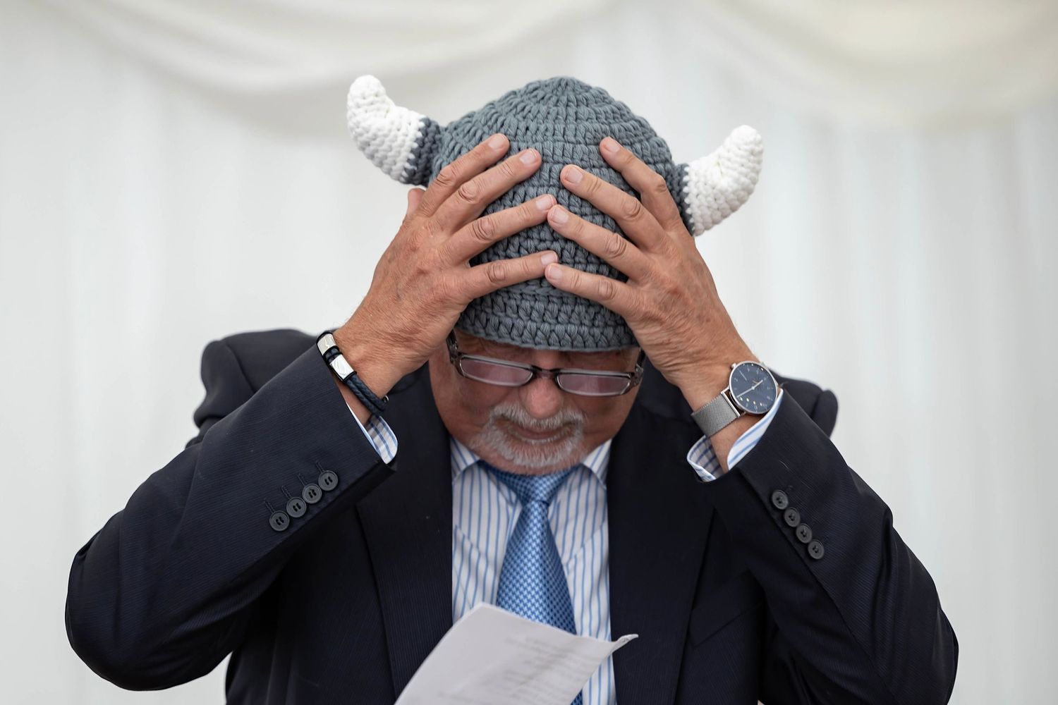 A person in a business suit and tie holds their head in frustration while sitting at a desk.