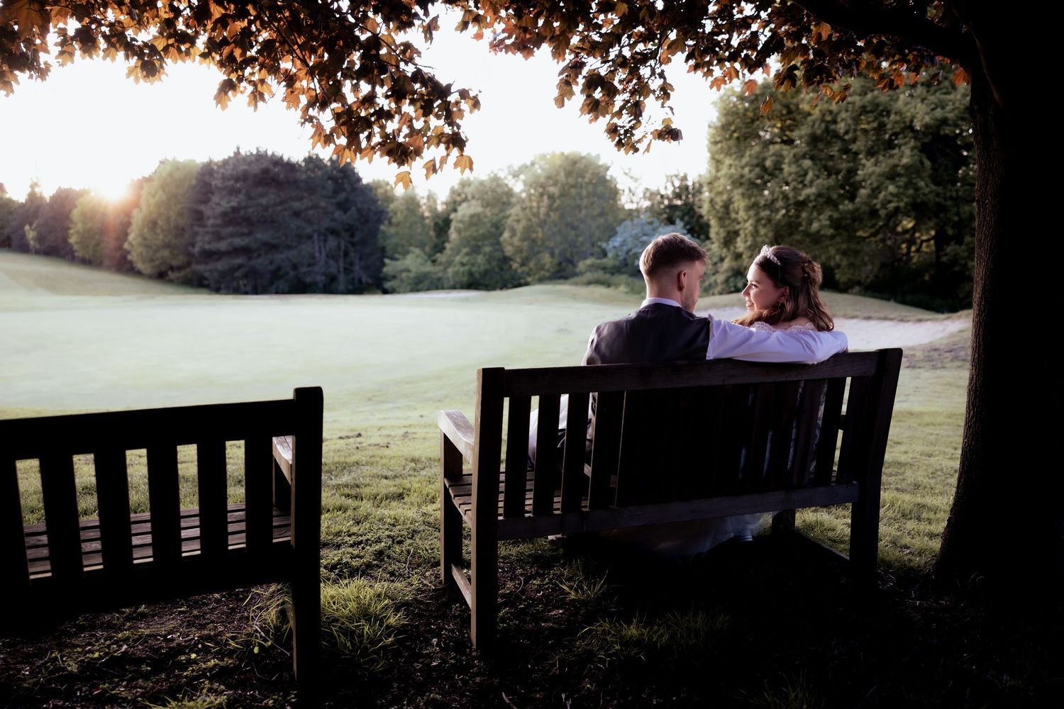Silhouettes of people sitting on park benches at sunset create a romantic outdoor scene.